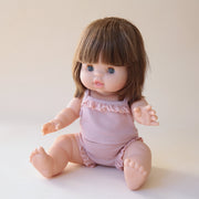 A baby doll with blue eyes, straight dark brown hair that is about shoulder length with bangs and wearing a light pink tank top set not included.
