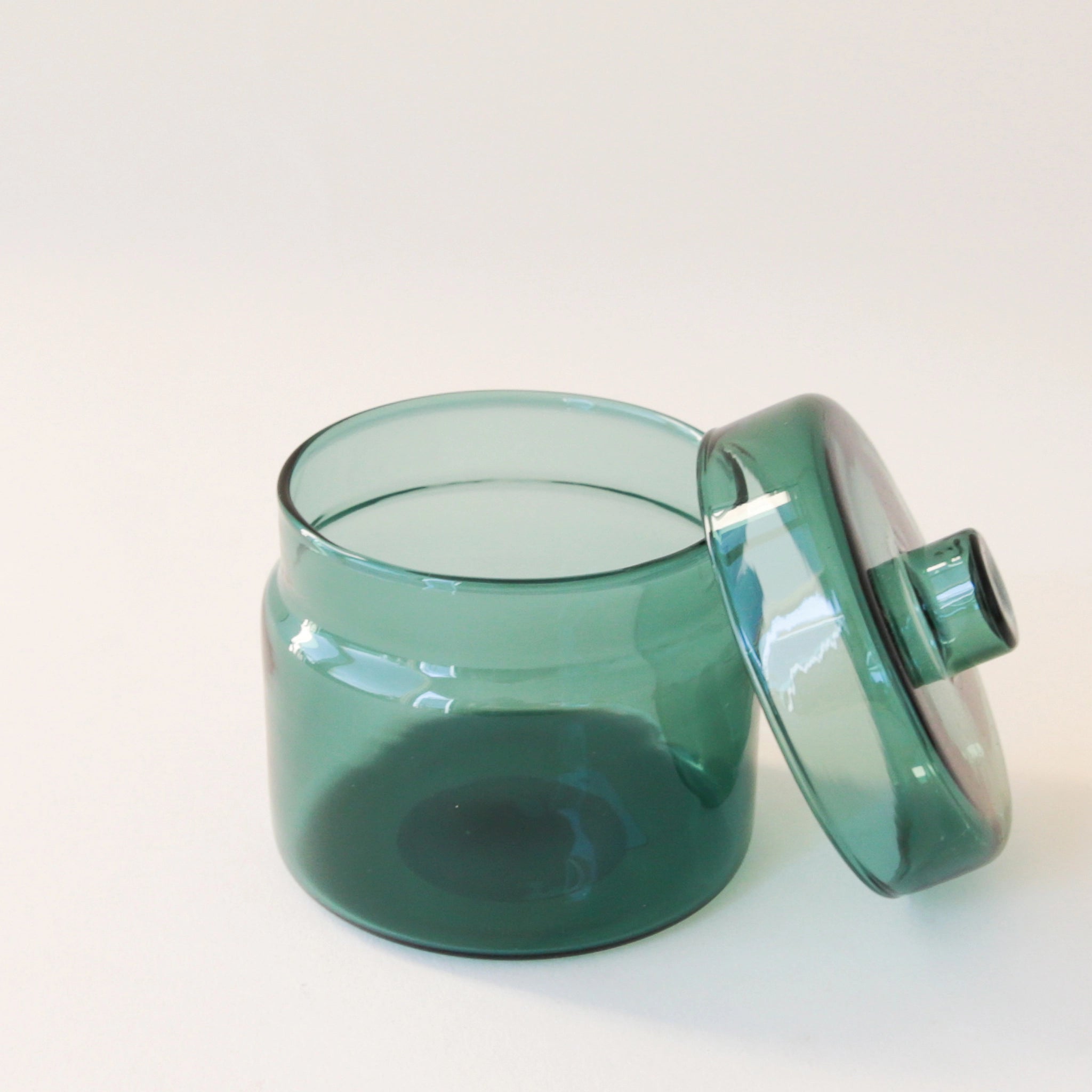 A round glass teal jar with a coordinating glass lid and a round but flat knob on top.