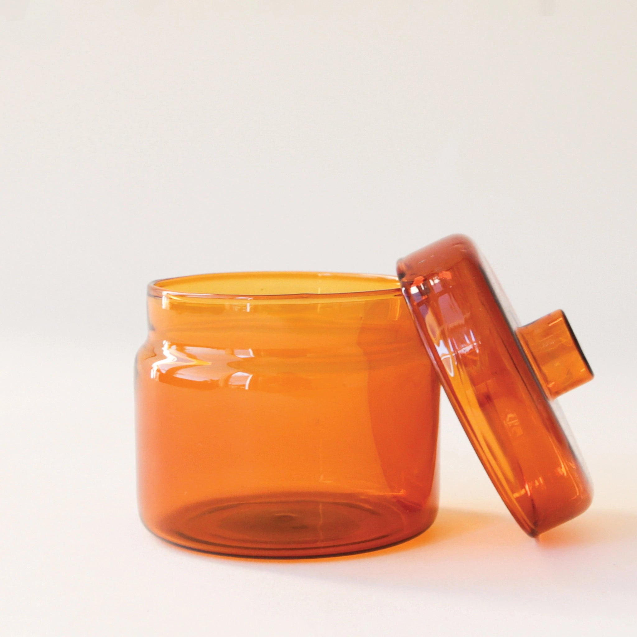 A round glass amber jar with a coordinating glass lid that has a round, flat knob on top.