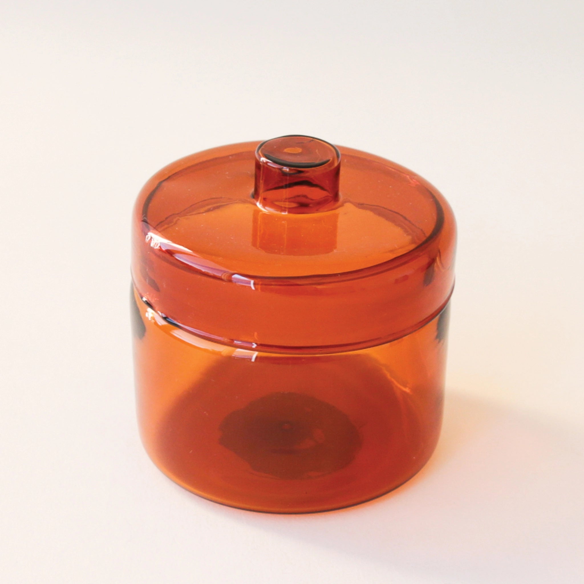 A round glass amber jar with a coordinating glass lid that has a round, flat knob on top.