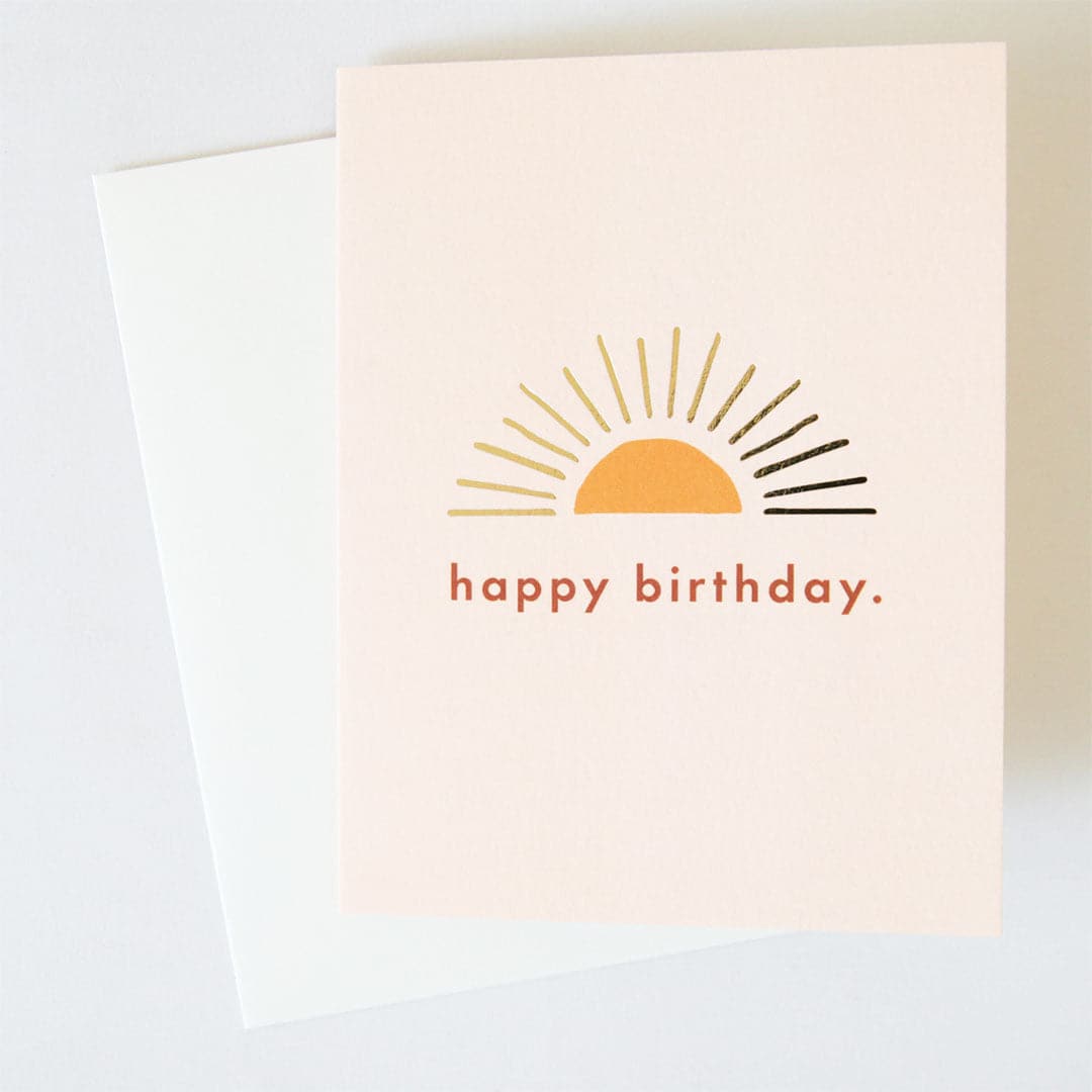 Ivory greeting card with yellow and gold foil sun illustration, &quot;happy birthday&quot; in orange text, and a white envelope.