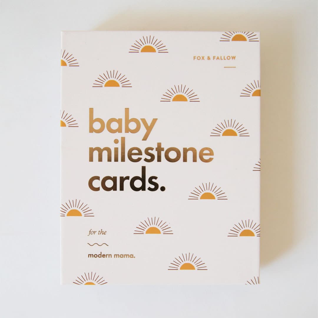 Ivory book with gold sun illustration and gold foil text "Baby Milestone Cards - For the modern mama"