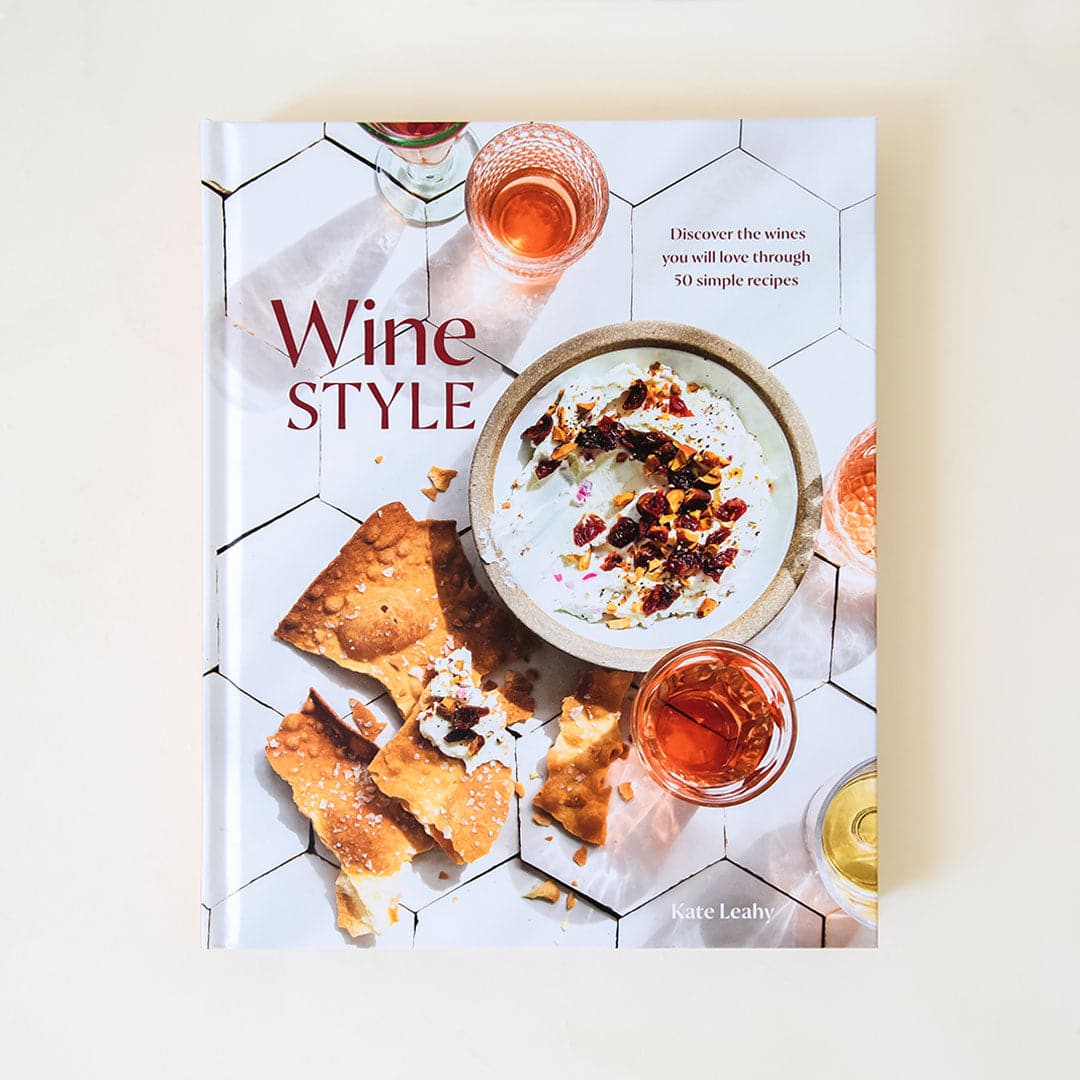 Hard covered cookbook titled 'Wine Style: Discover the wines you will love through 50 simple recipes' in red lettering. Book cover features brittle salted crackers and dip along side wine-filled cocktail glasses against white modern tiled. 