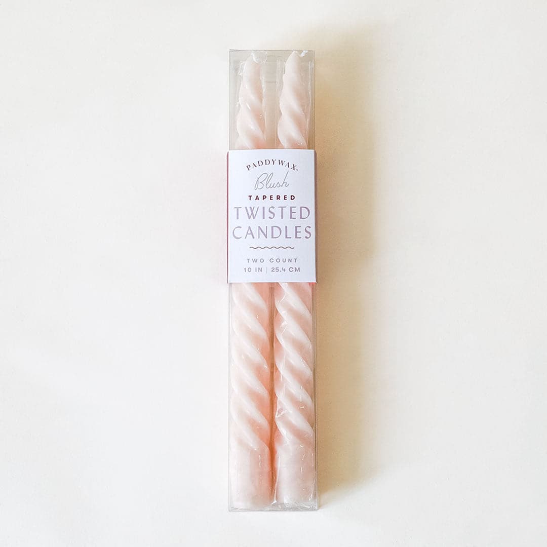 Pair of two blush pink, twisted taper candles with white cotton wicks lay beside each other fasted in clear plastic packaging. The packaging reads &#39;Blush Tapered Twisted Candles&#39;