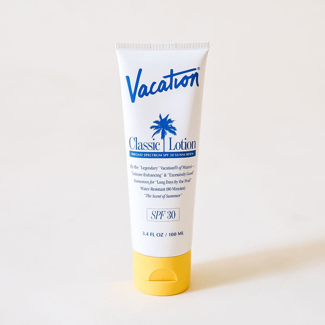 On a white background is a white squeeze tube of sunscreen with a yellow lid and a blue text that reads, "Vacation Classic Lotion SPF 30" along with a blue palm design in the center. 