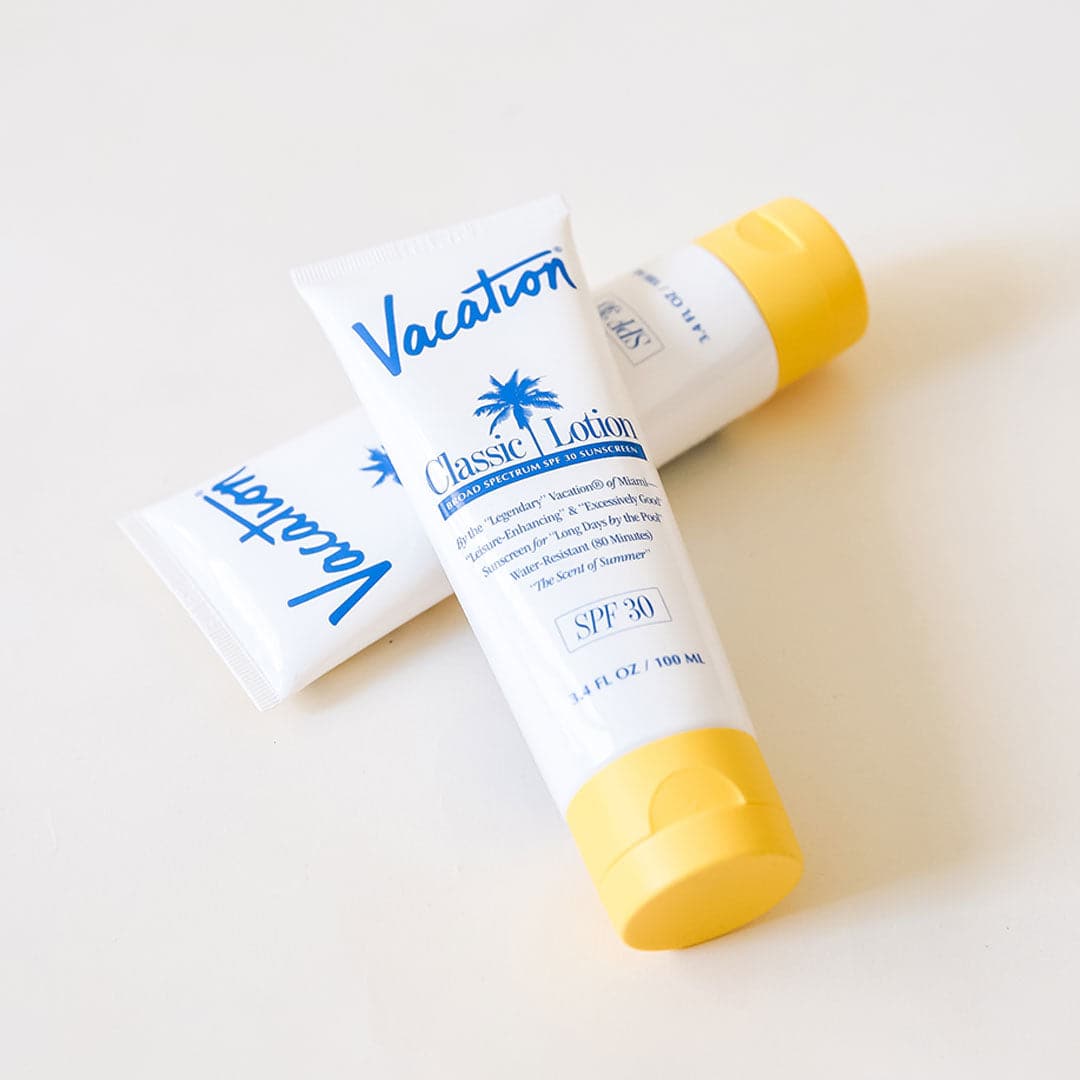On a white background is a white squeeze tube of sunscreen with a yellow lid and a blue text that reads, &quot;Vacation Classic Lotion SPF 30&quot; along with a blue palm design in the center.