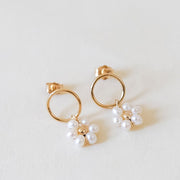 On a cream background is a pair of hoop earrings with a pearl daisy hanging off the edge. 