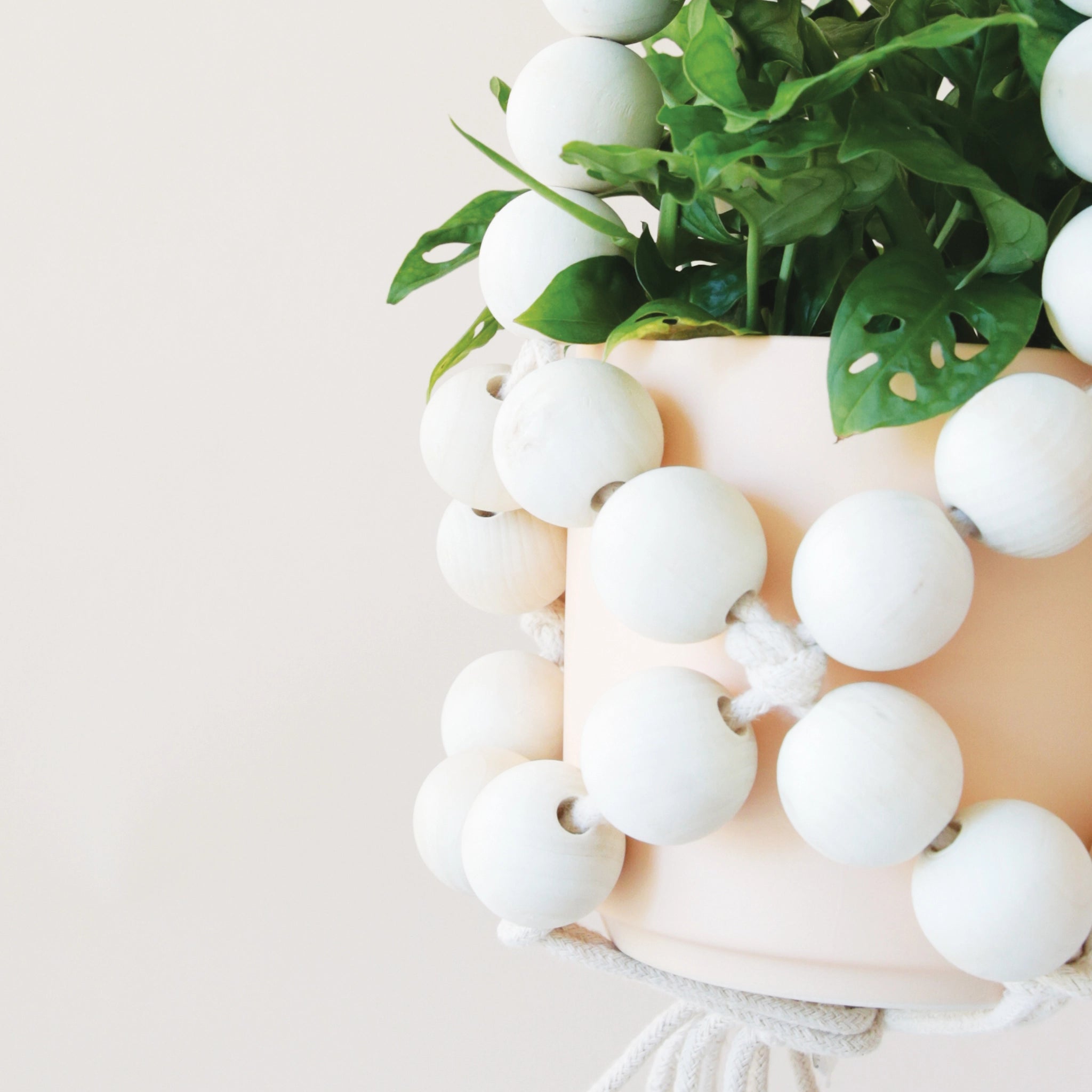 A plant hanger made of large round wooden beads forming a basket shape and coming together at the top to hang.