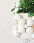 A plant hanger made of large round wooden beads forming a basket shape and coming together at the top to hang.