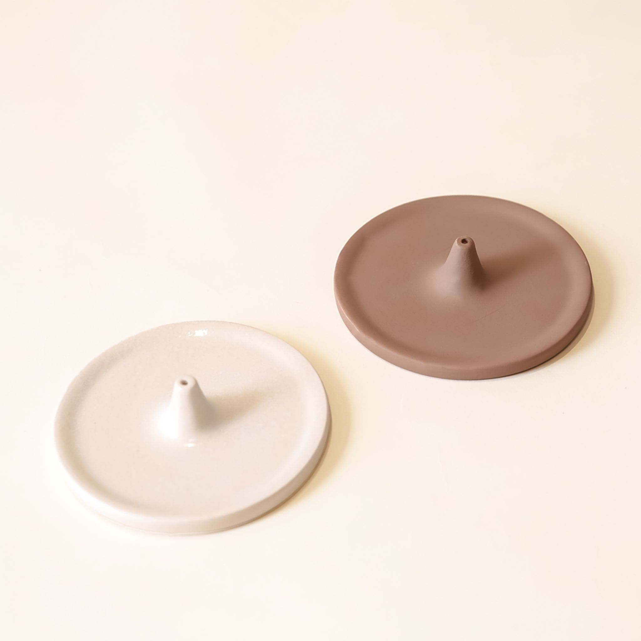 Two separate incense holders. They have a circular shape with a point in the center that is raised with a hole to place your incense in. There is a creamy white and a brown option.