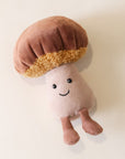 A soft suede stuffed animal in the shape of a mushroom with light brown cap with curly soft gold underneath, a tan colored stalk with smiley face and brown floppy legs.