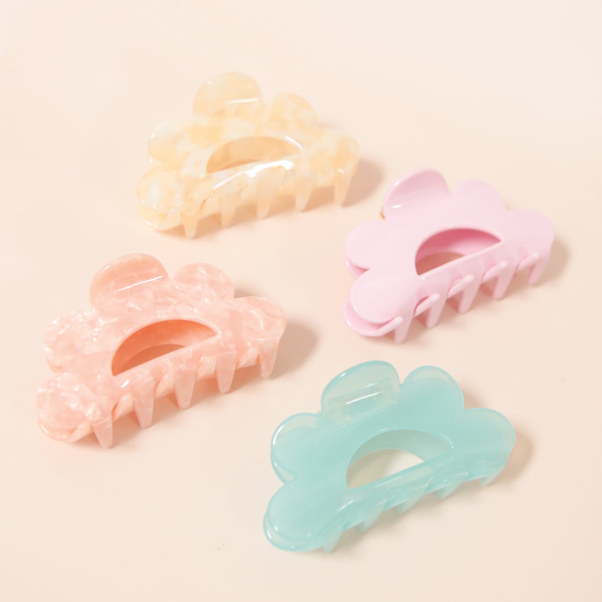 Four different colored scalloped claw clips. There is an ivory, a pink, a scallop and then a light blue. 