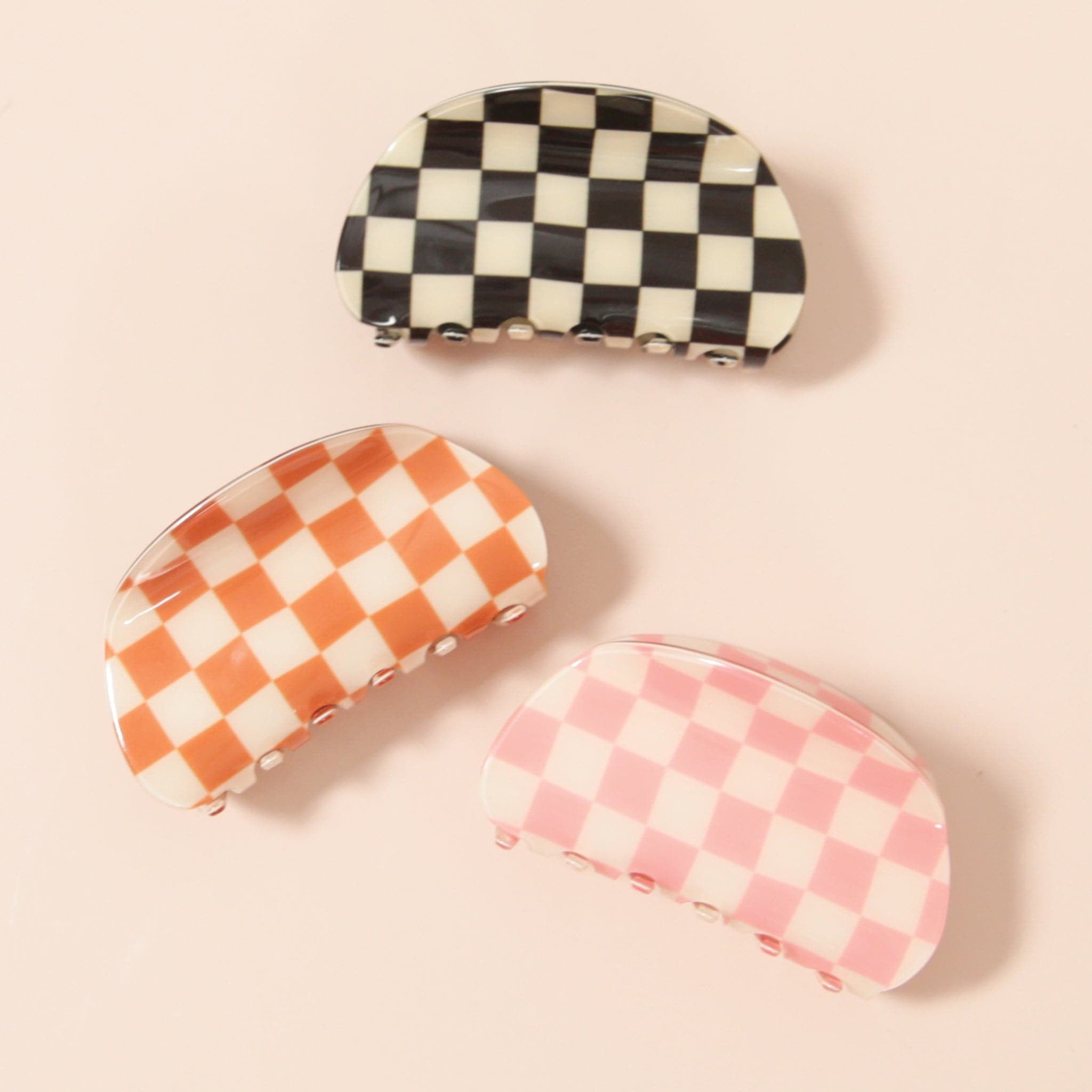 On a white background is three clips, one orange and white checkered, one white and pink, and the other black and white. 