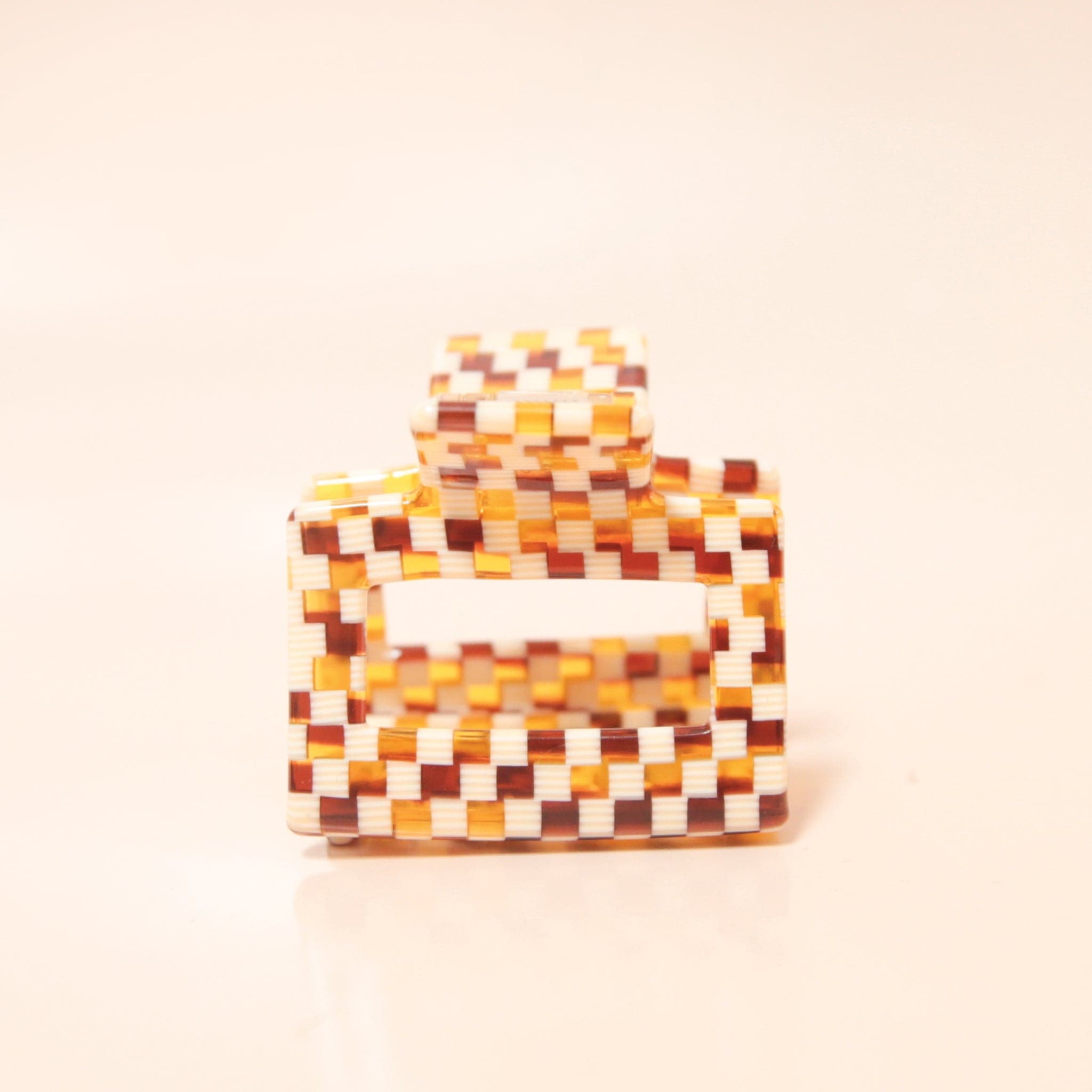 A white and brown acrylic checkered claw hair clip with a square shape and two simple geometric cutouts.