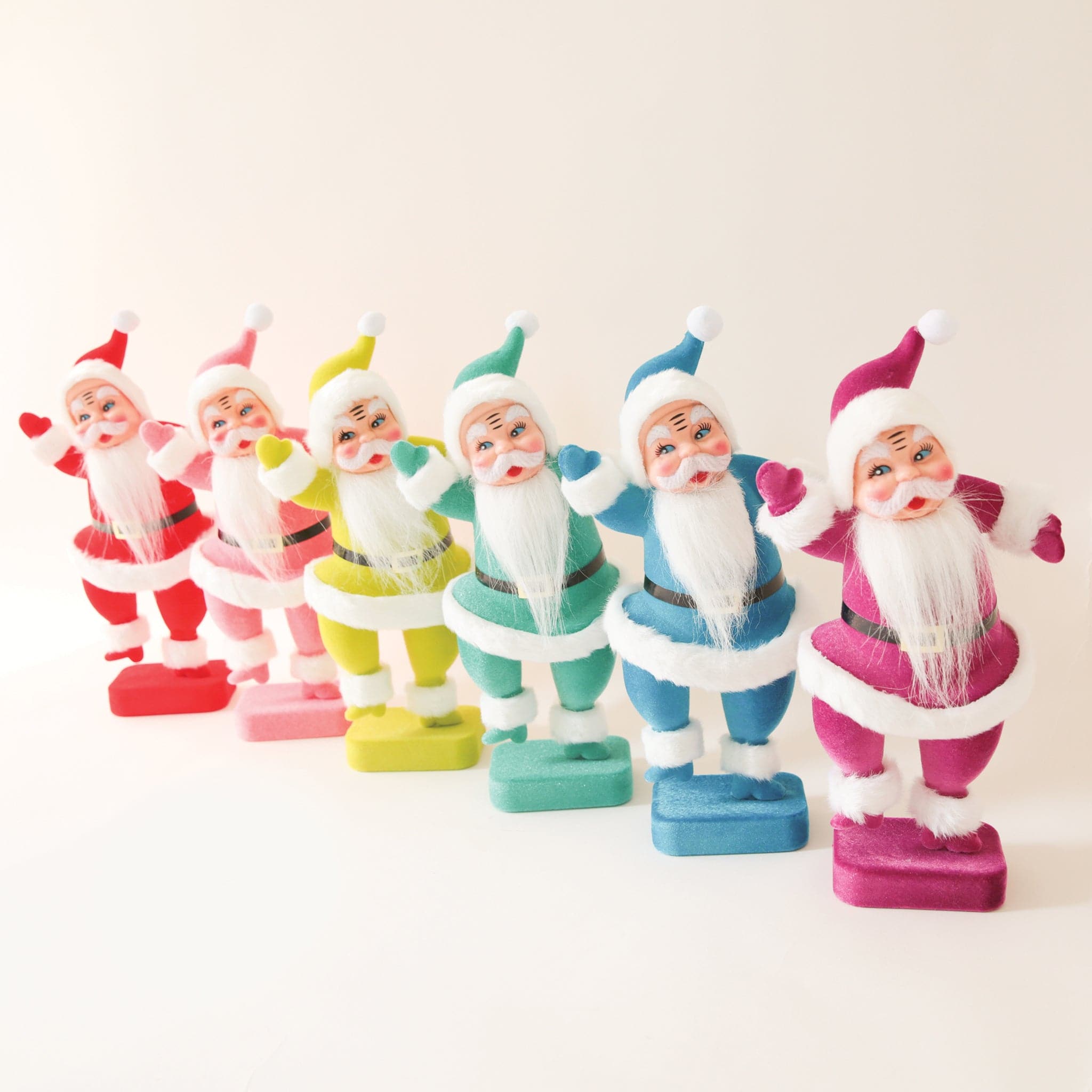 A plastic Santa figurine with a teal suit on with fuzzy cuffs and hat next to all the other colors available. 