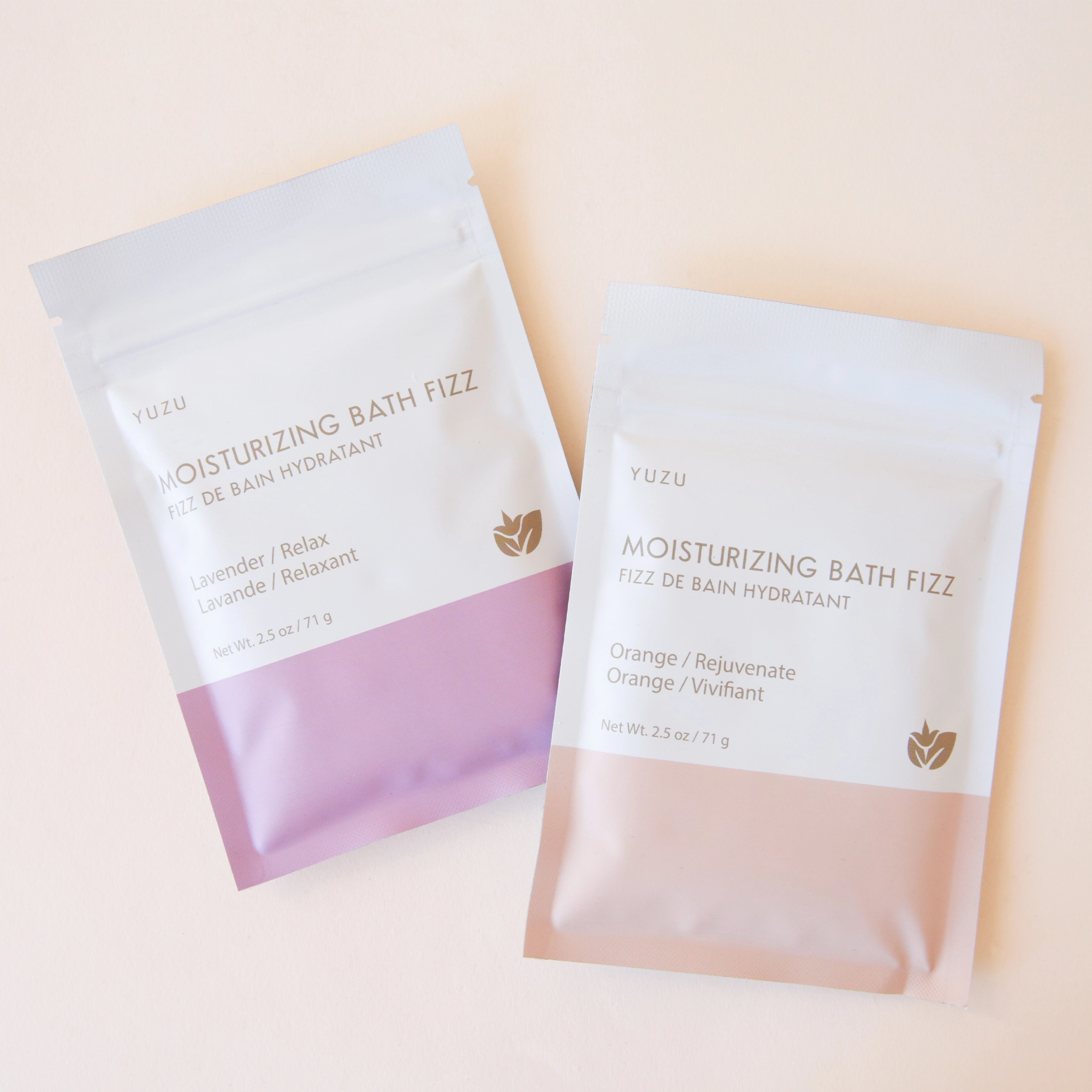 A packet of bath salts with the bottom half a light pink color and the top half white along with text on the front that reads, "Moisturizing Bath Fizz, Orange / Rejuvenate" photographed with the Lavender scent that's also available on our website.