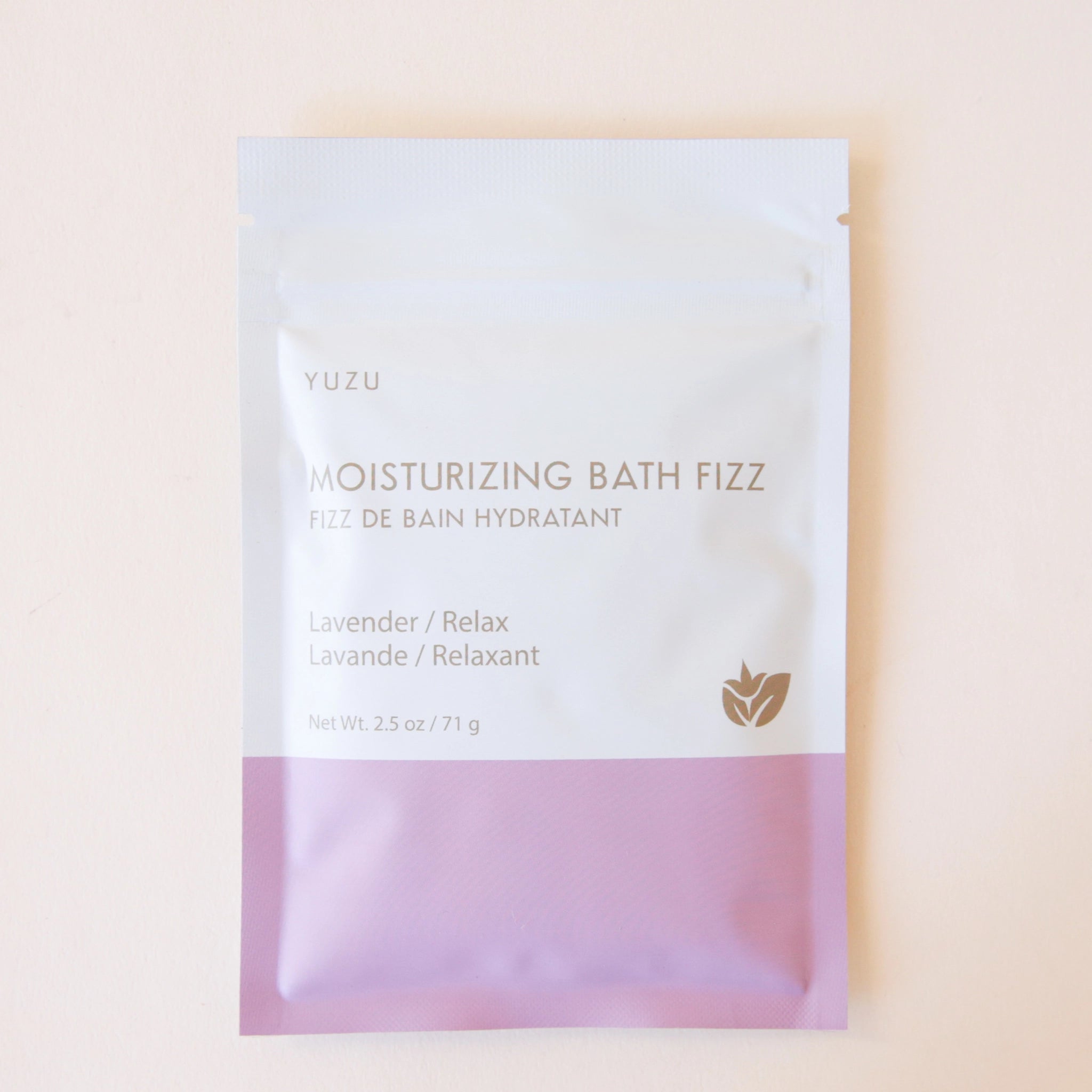 A packet of bath salts with the bottom half a light pink color and the top half white along with text on the front that reads, "Moisturizing Bath Fizz, Lavender / Relax".