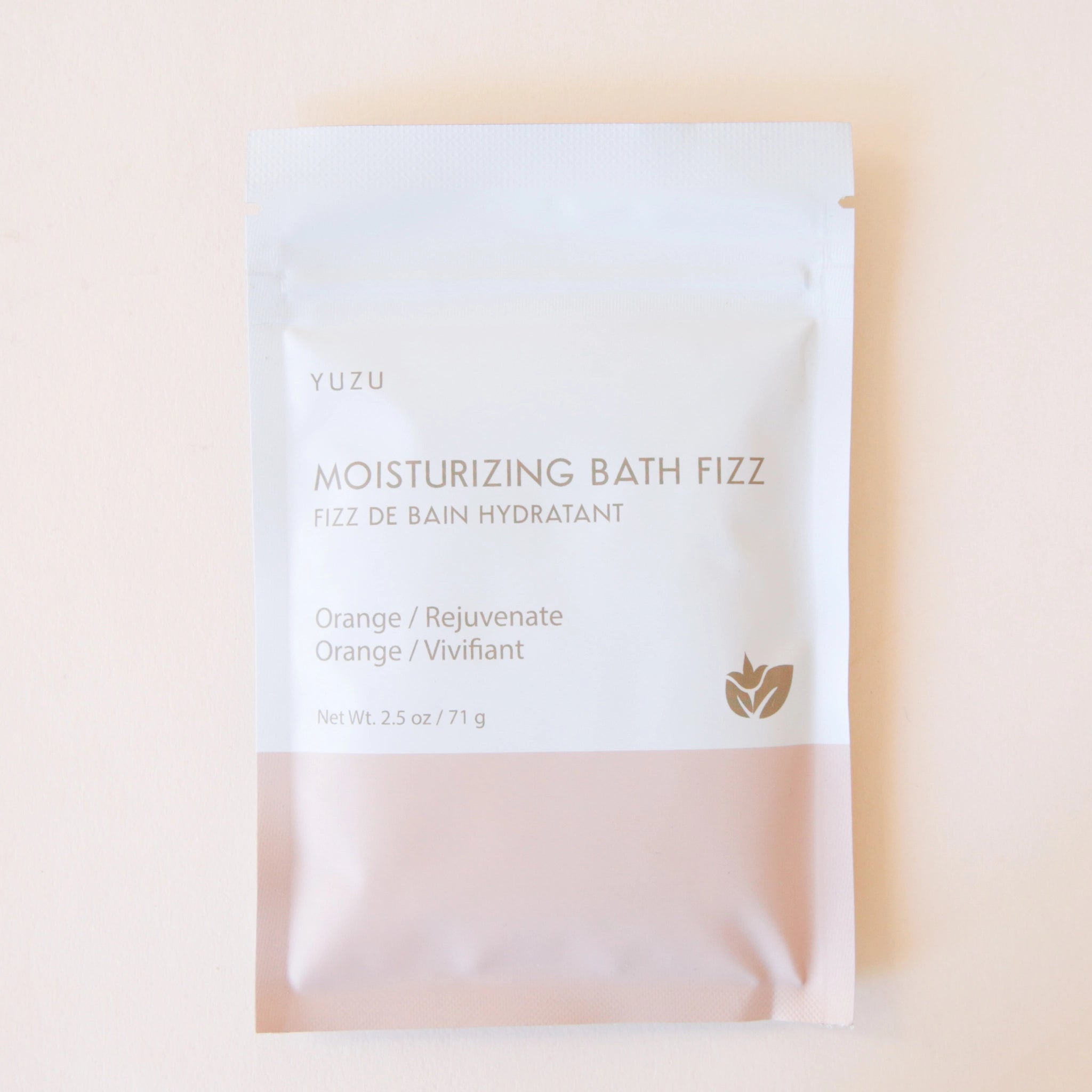 A packet of bath salts with the bottom half a light pink color and the top half white along with text on the front that reads, "Moisturizing Bath Fizz, Orange / Rejuvenate".