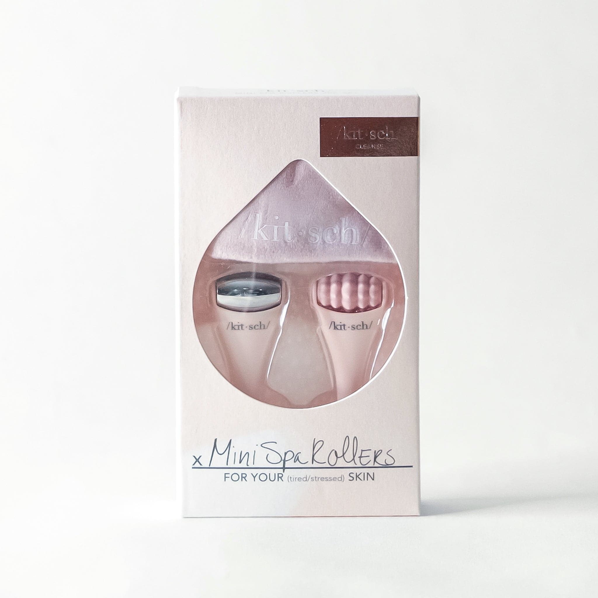 On a white background is a light pink packaging holding two mini facial massage tools. One with a smooth stainless steel roller and the other with a more textured light pink roller. 
