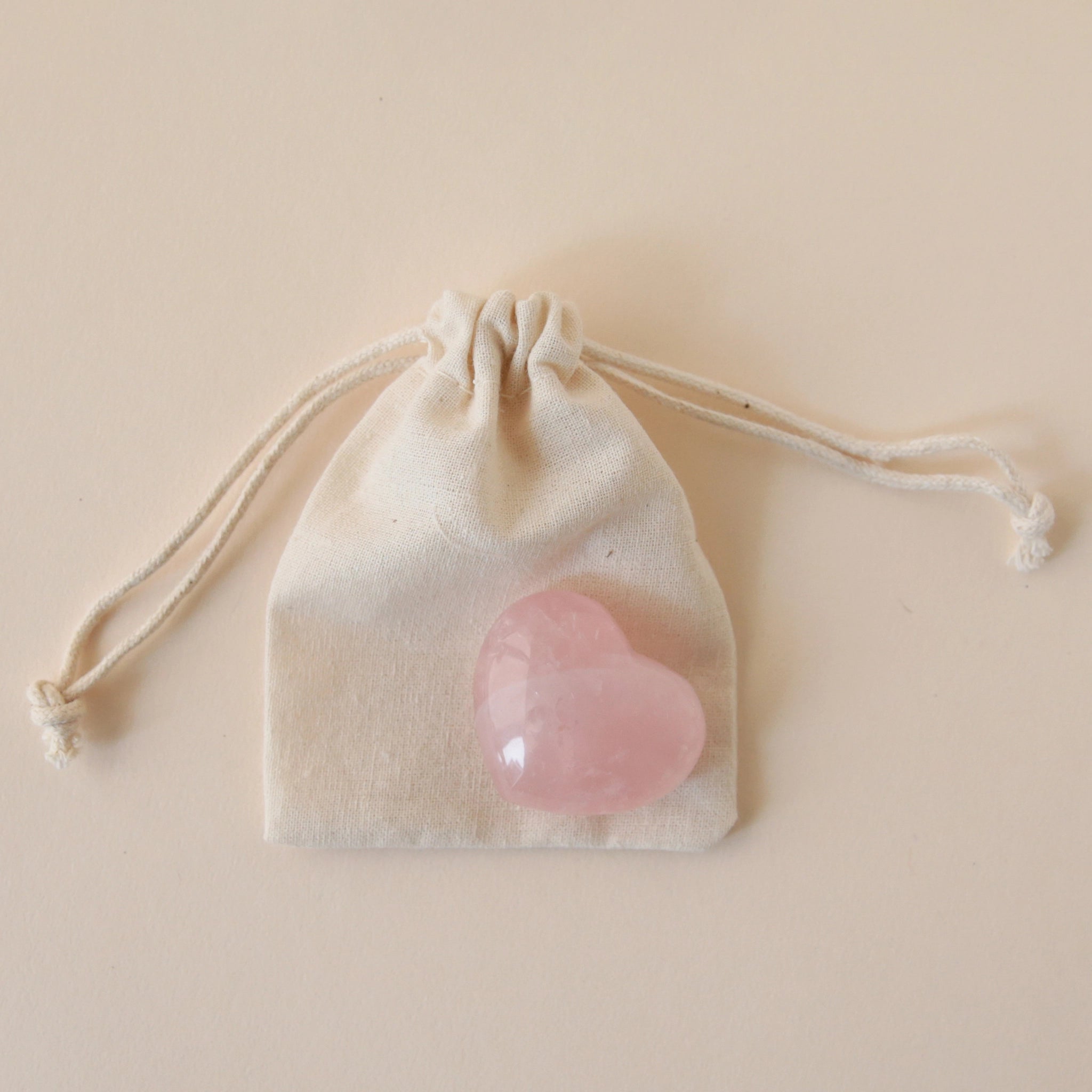 A tan muslin bag with a rose quartz stone int he shape of a heart.