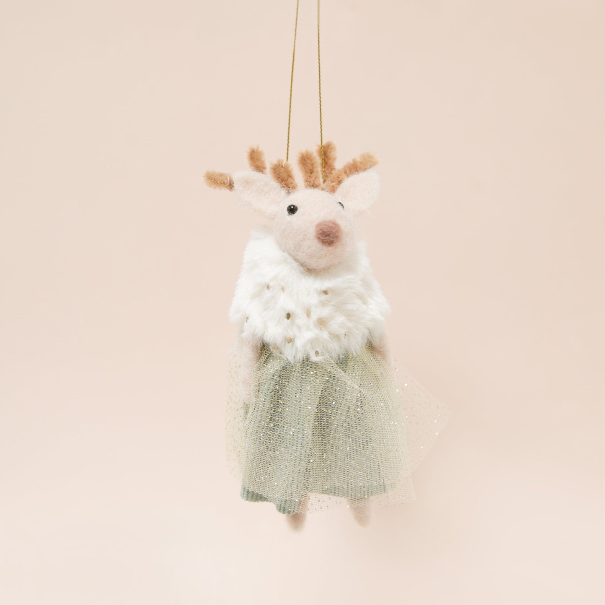Against a peachy background is a felted deer ornament in a faux fur shall and a green tulle dress.