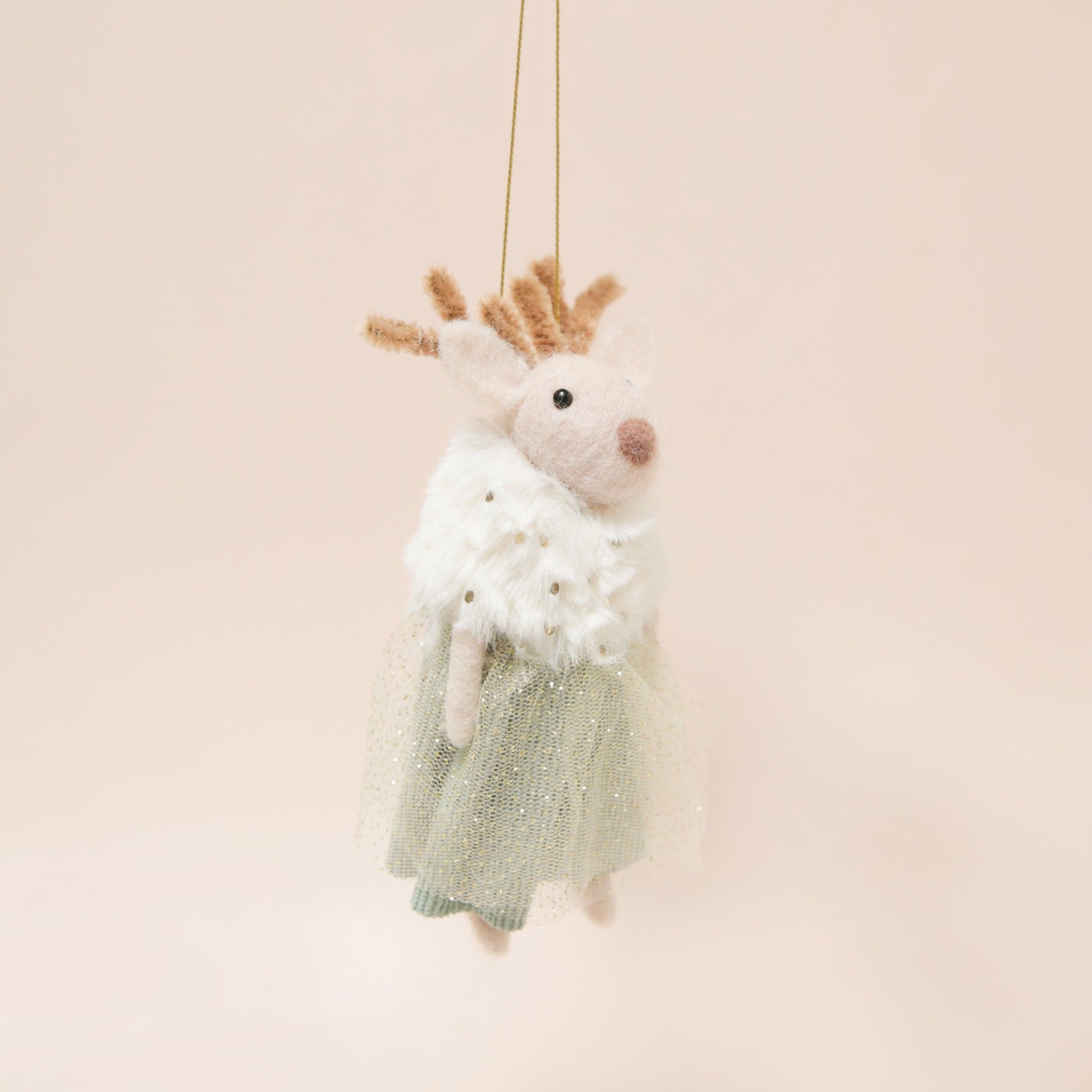 Against a peachy background is a felted deer ornament in a faux fur shall and a green tulle dress.