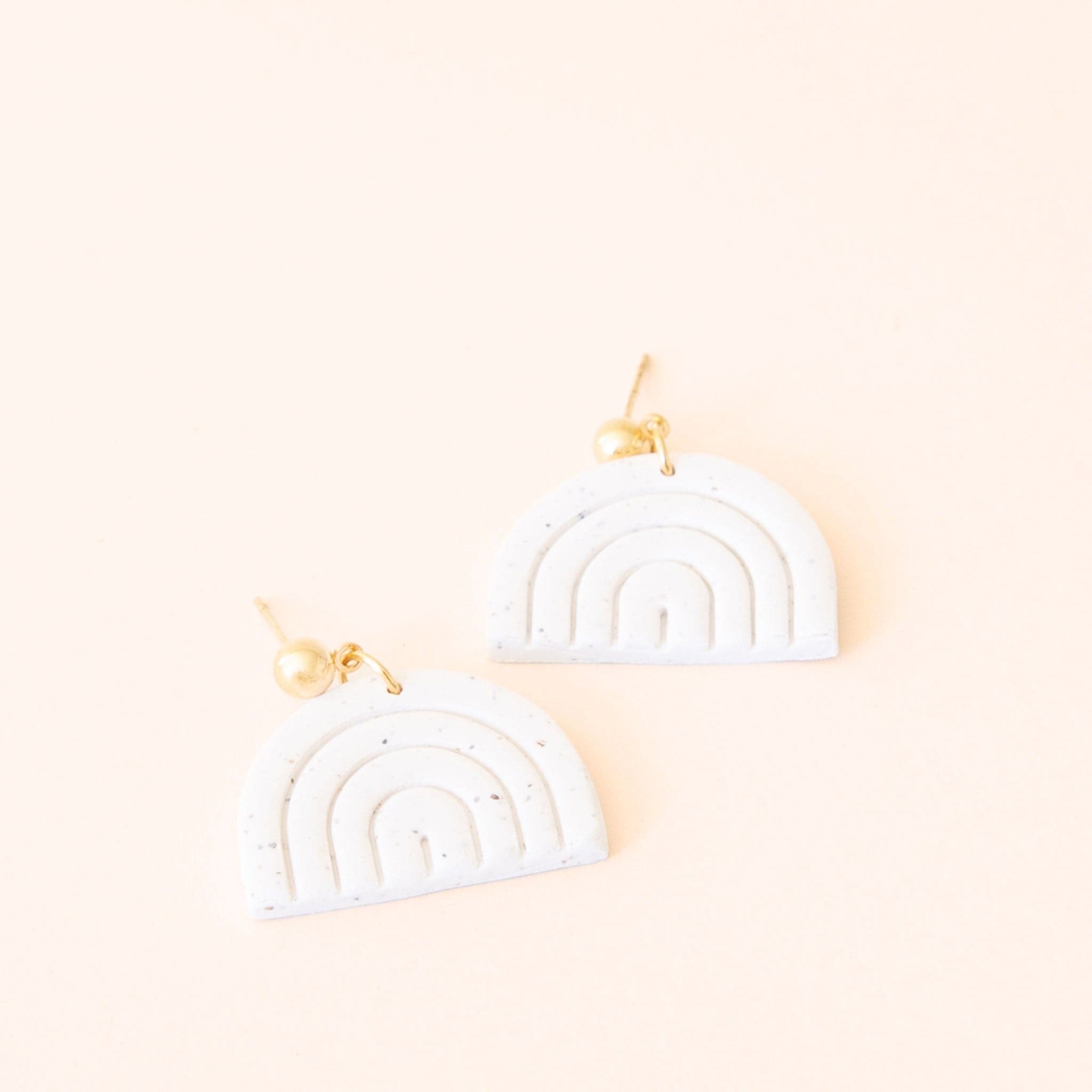 Pair of earrings made of two clay white rainbows. Each earring is attached to the post with a small gold hoop. 