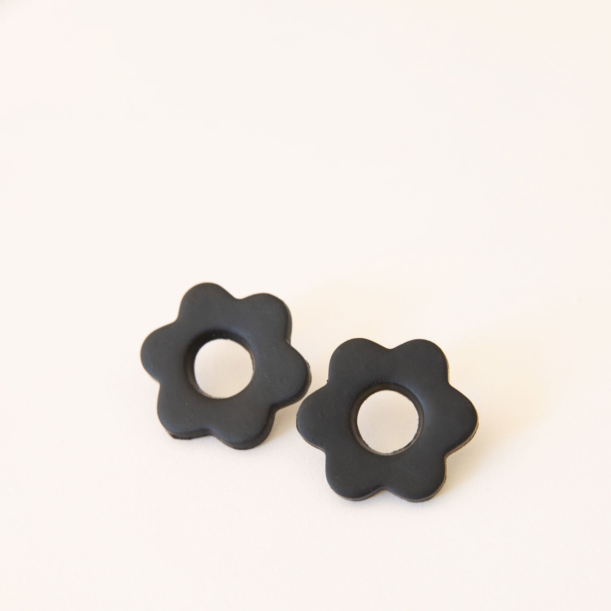 Pair of two solid black flower earrings. Each flower has a hole in its center and is made of polymer clay. 
