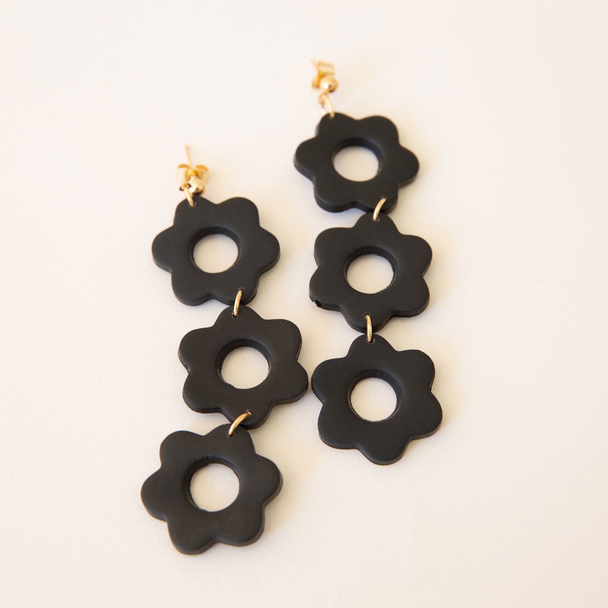 Pair of two earrings with three dangling black flowers made of black polymer clay. The flowers are bound together in a row with small gold hoops.  