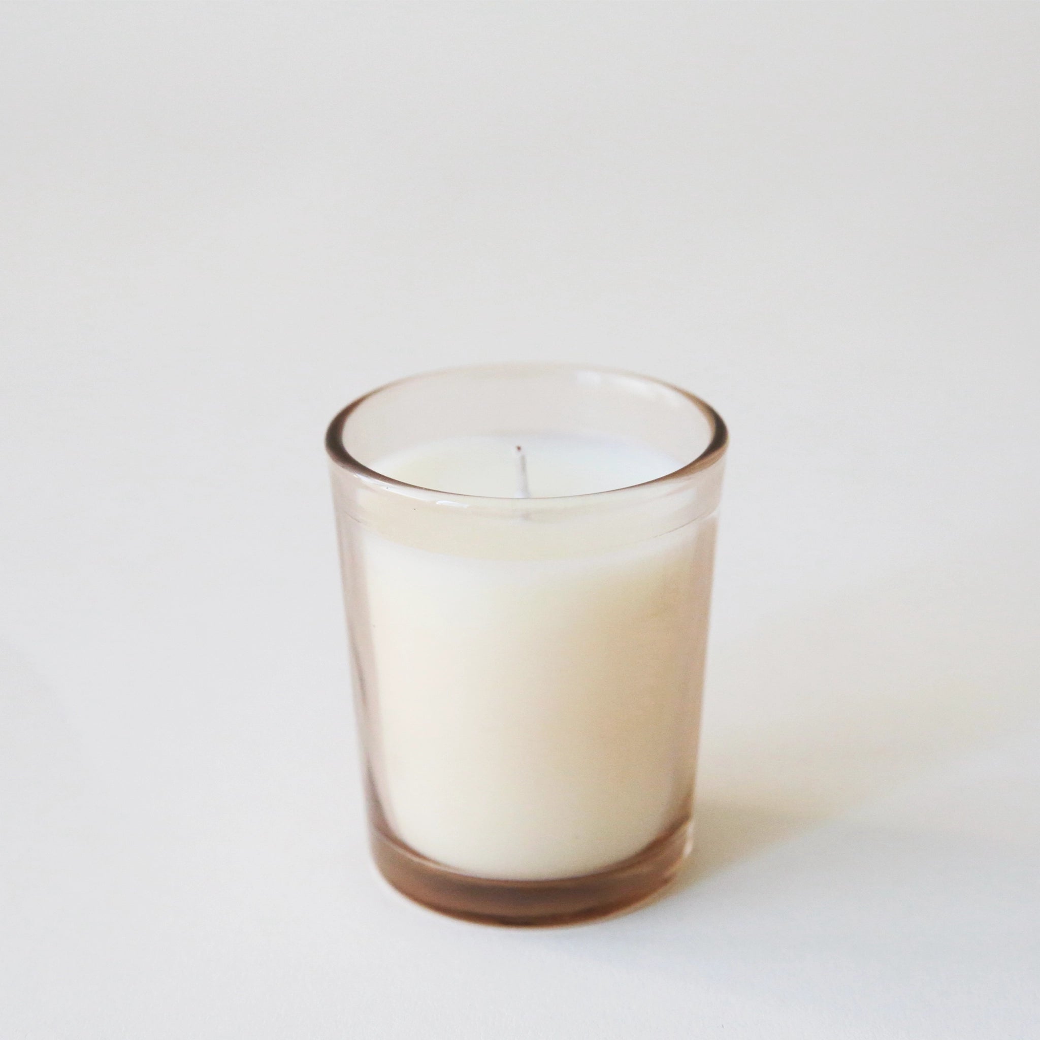A tan glass jar candle with a white wax candle inside.