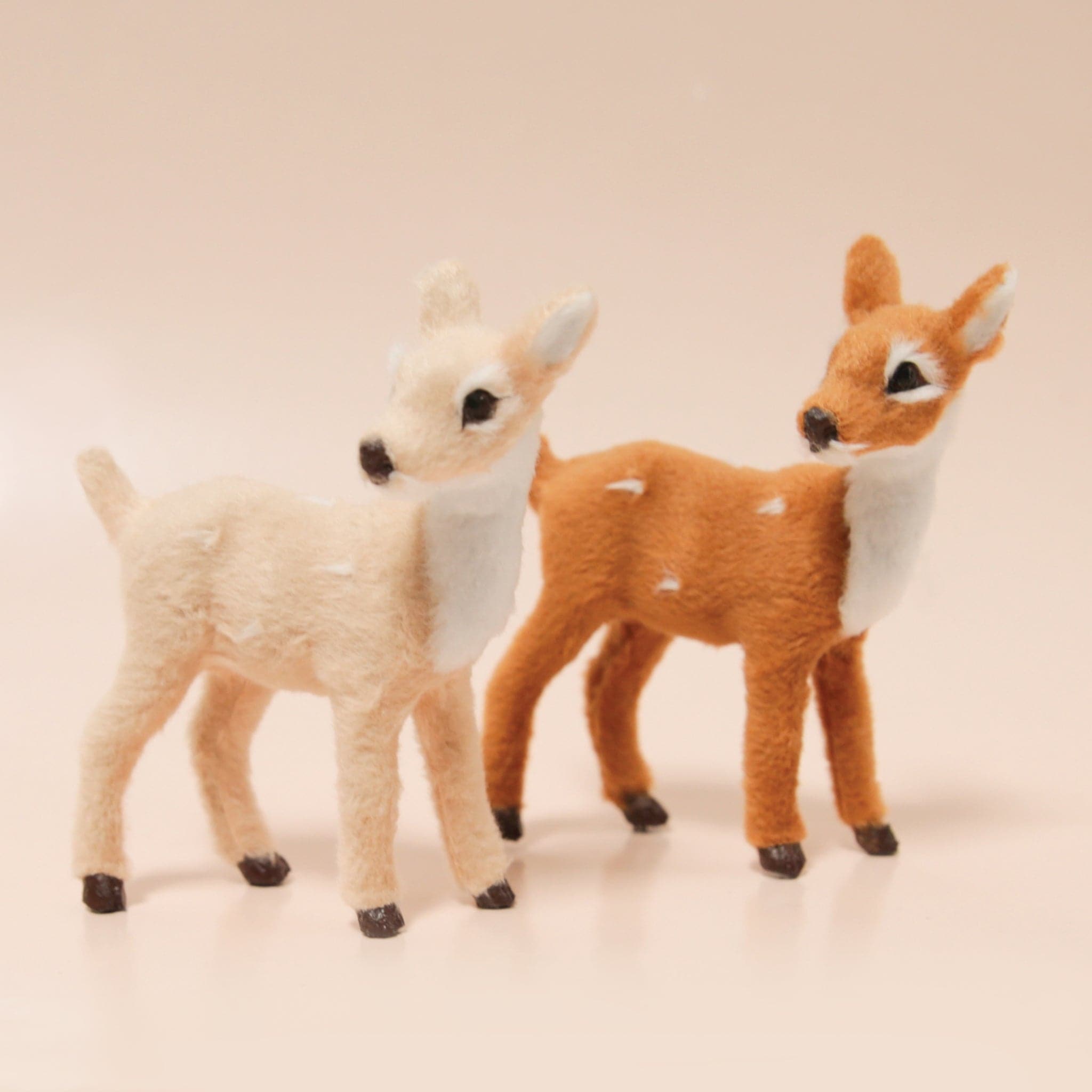 One cream and one brown reindeer fawn figures sit atop a peach background