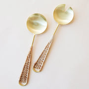 A set of salad serving utensils with a gold scoop and a woven rattan handle.