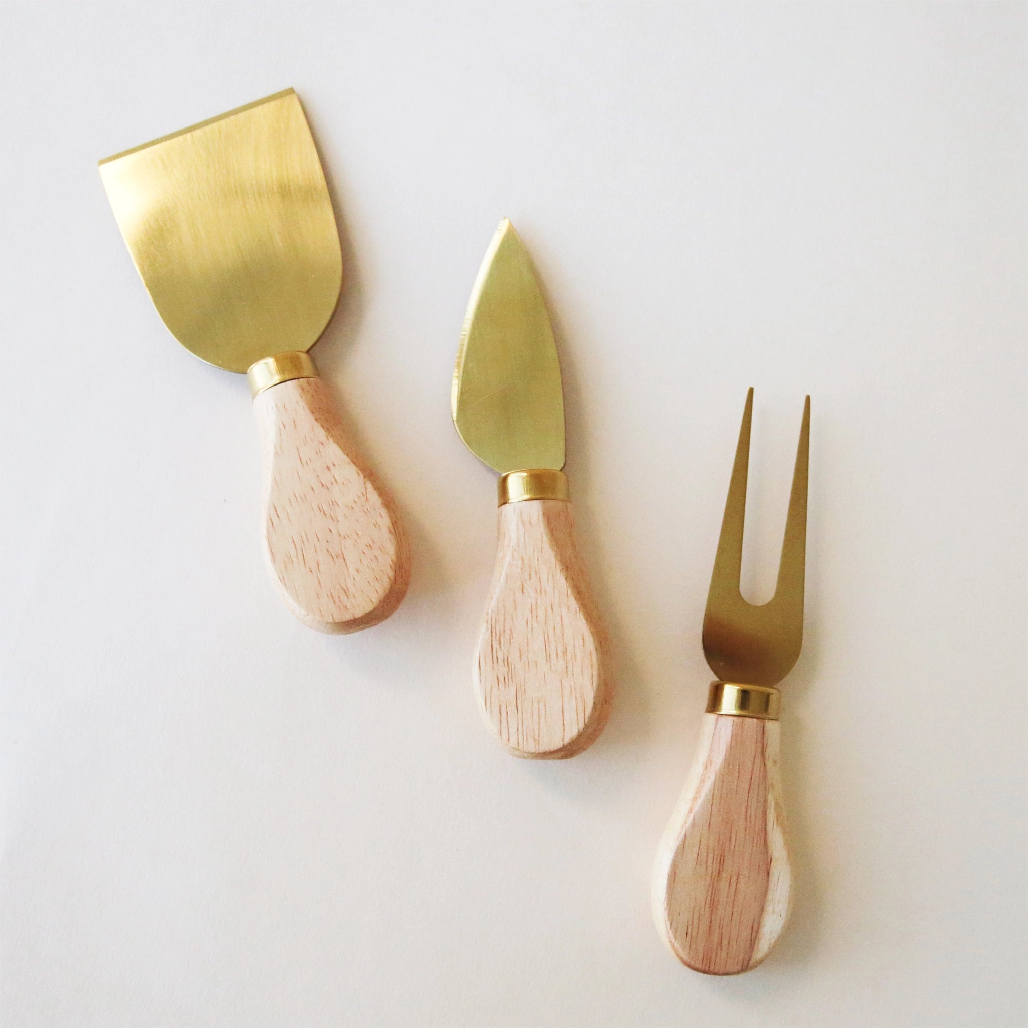 A set of three cheese utensils with oak handles and gold utensils.
