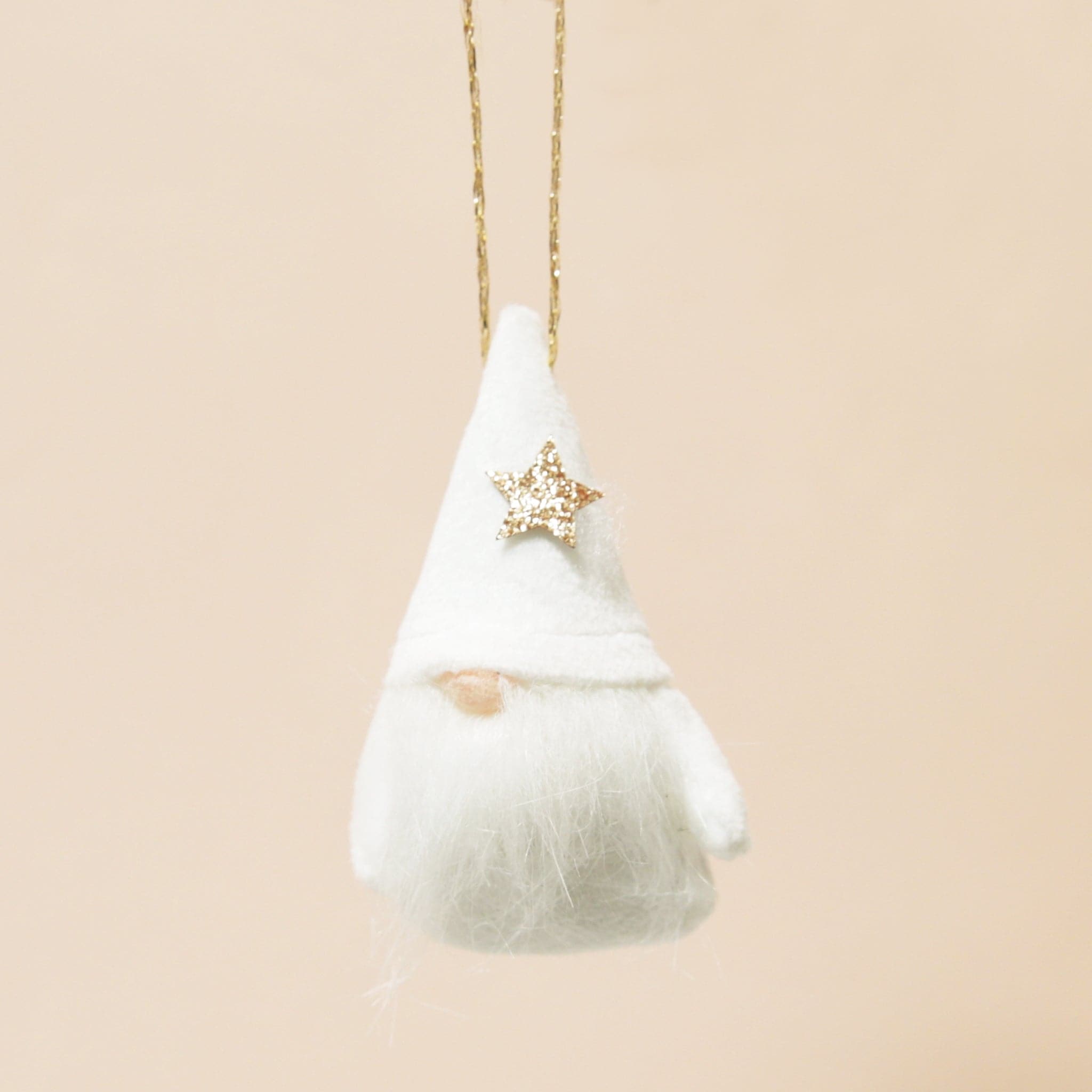 A plush white gnome ornament with a gold star and beard on a neutral ground.