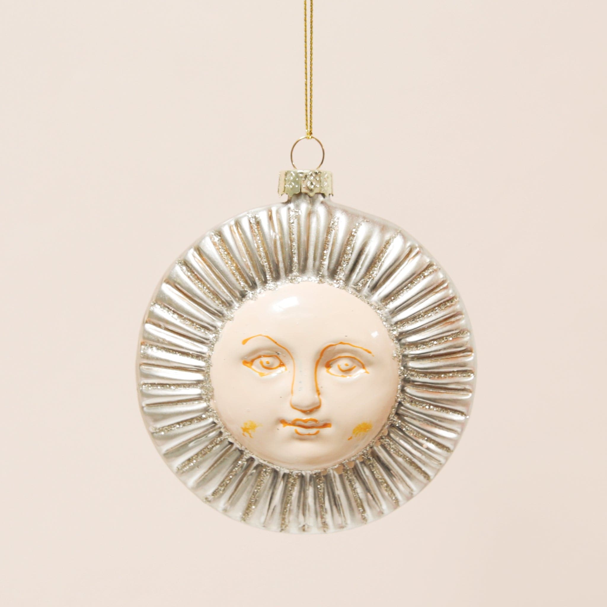 A round glass silver sun ornament with glitter detailing and a face in the center.