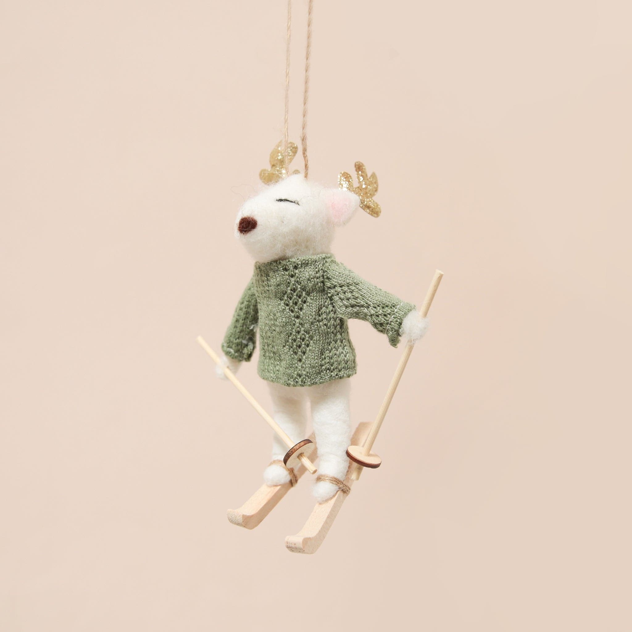 A white felt deer ornament in a green sweater on a pair of light wood skis as well as holding ski poles. The deers antlers are gold with sparkles.