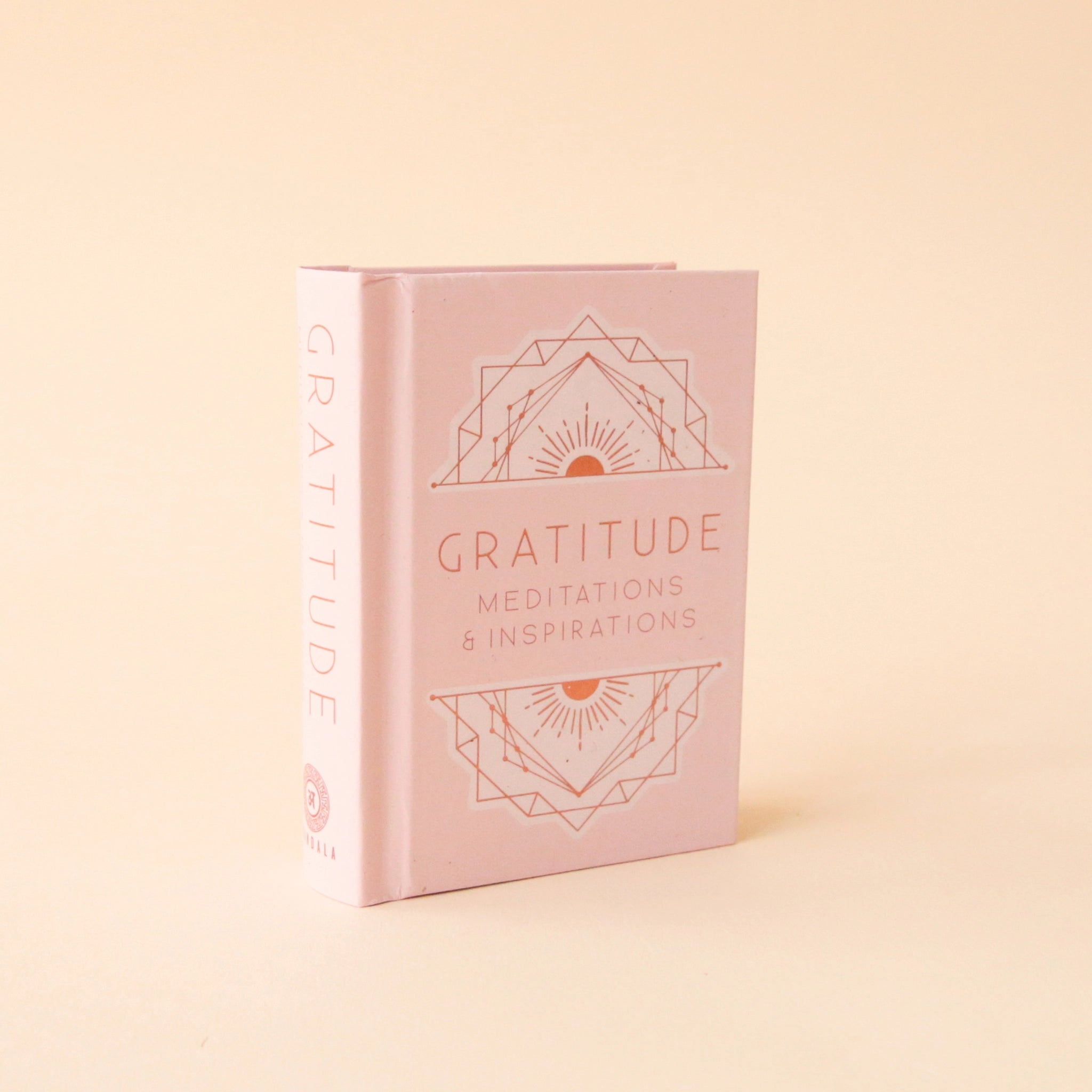 A small pink book that says, "Gratitude Meditations & Inspirations" in light pink on the front cover as well as s geometric illustration above and below the text.