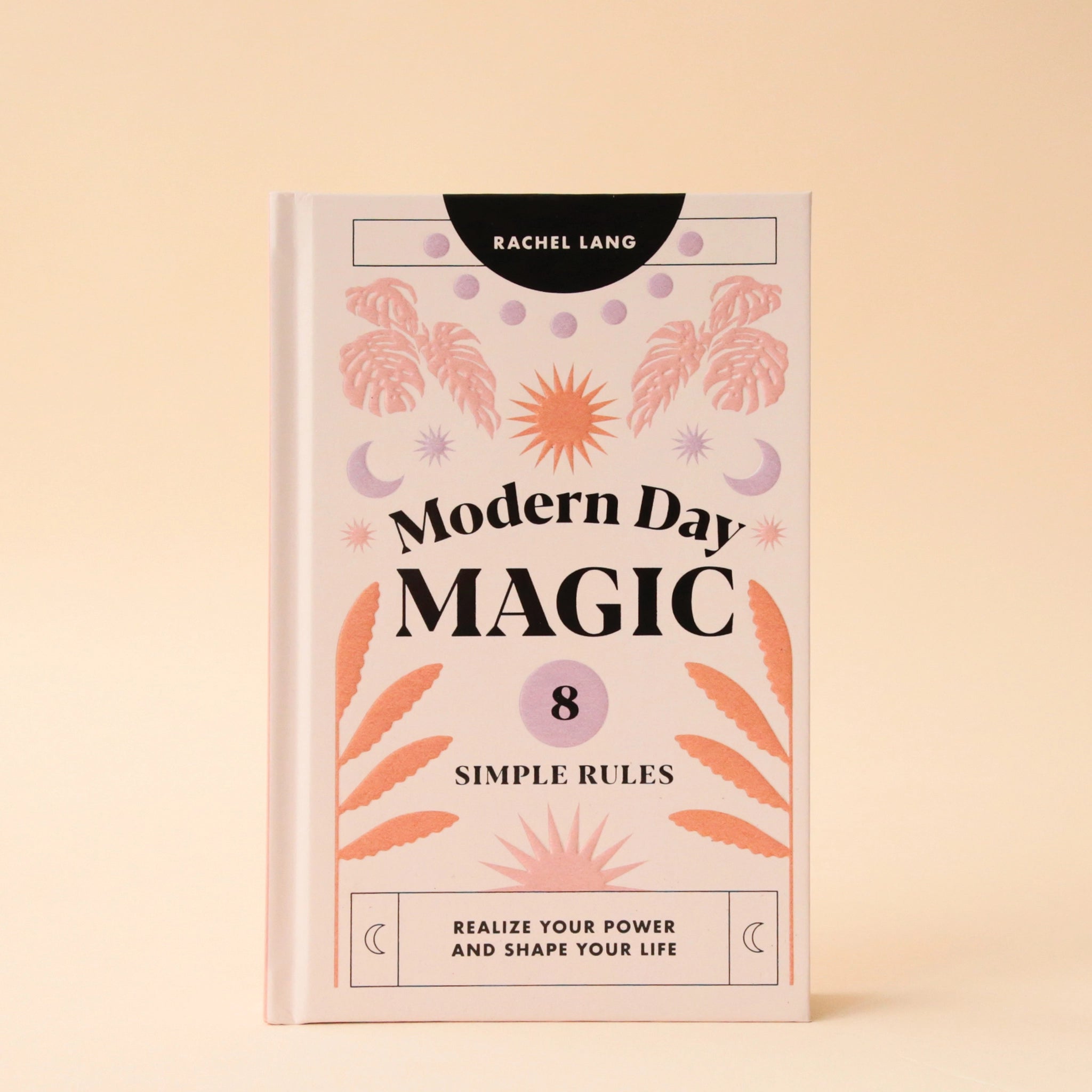 A light pink book cover with pink, lavender and orange foliage and sun and moon graphics along with black text that reads, "Modern Day Magic 8 Simple Rules Realize Your Power and Shape Your Life".