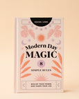 A light pink book cover with pink, lavender and orange foliage and sun and moon graphics along with black text that reads, "Modern Day Magic 8 Simple Rules Realize Your Power and Shape Your Life".