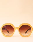Mustard yellow circular frame sunglasses with a brown lens and tortoise arms photographed in front of a peachy background.