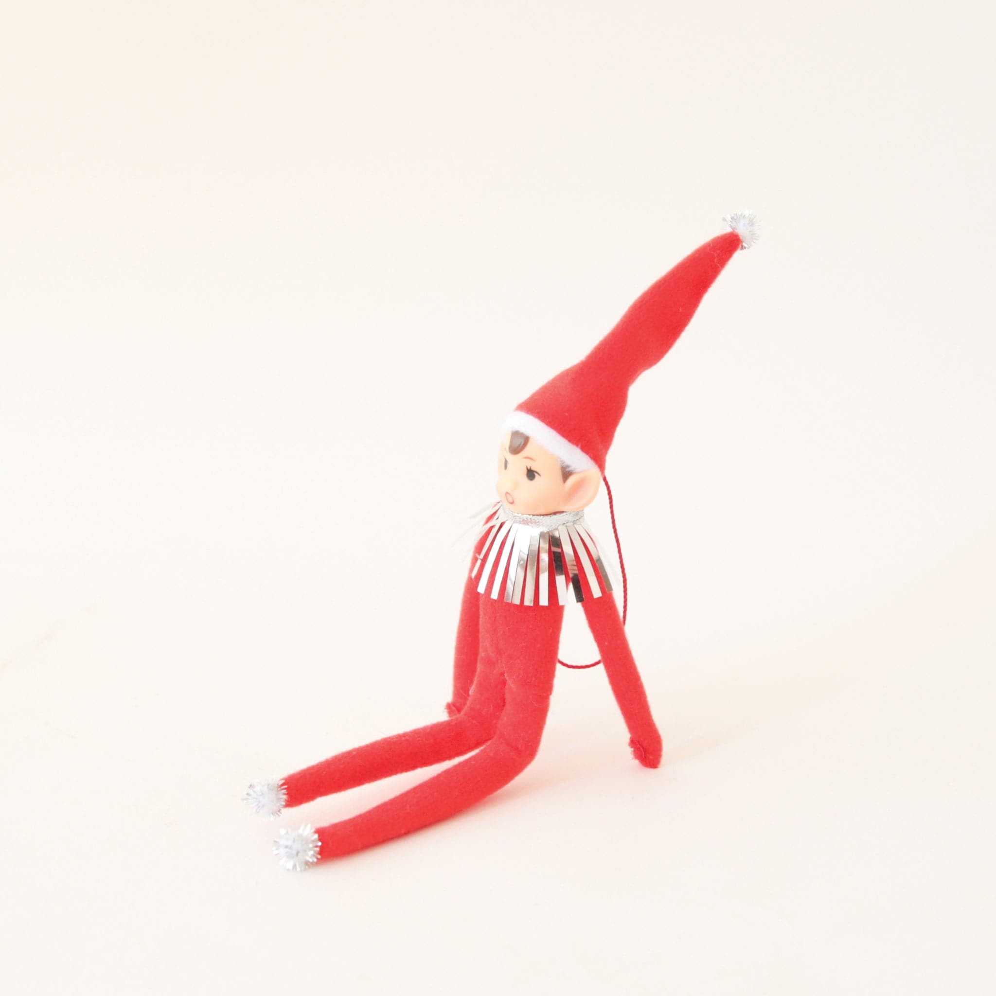 On a cream background is a red elf ornament with bendy arms and legs and a red loop for hanging.