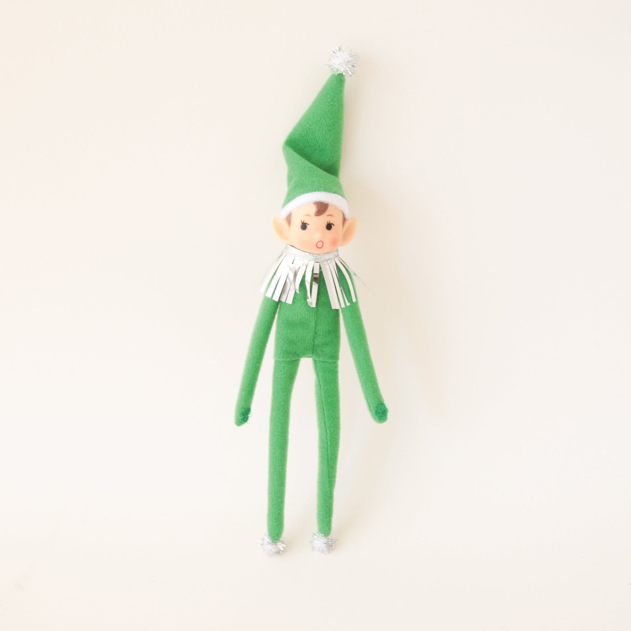 On a cream background is a green elf ornament with bendy arms and legs and a green loop for hanging.