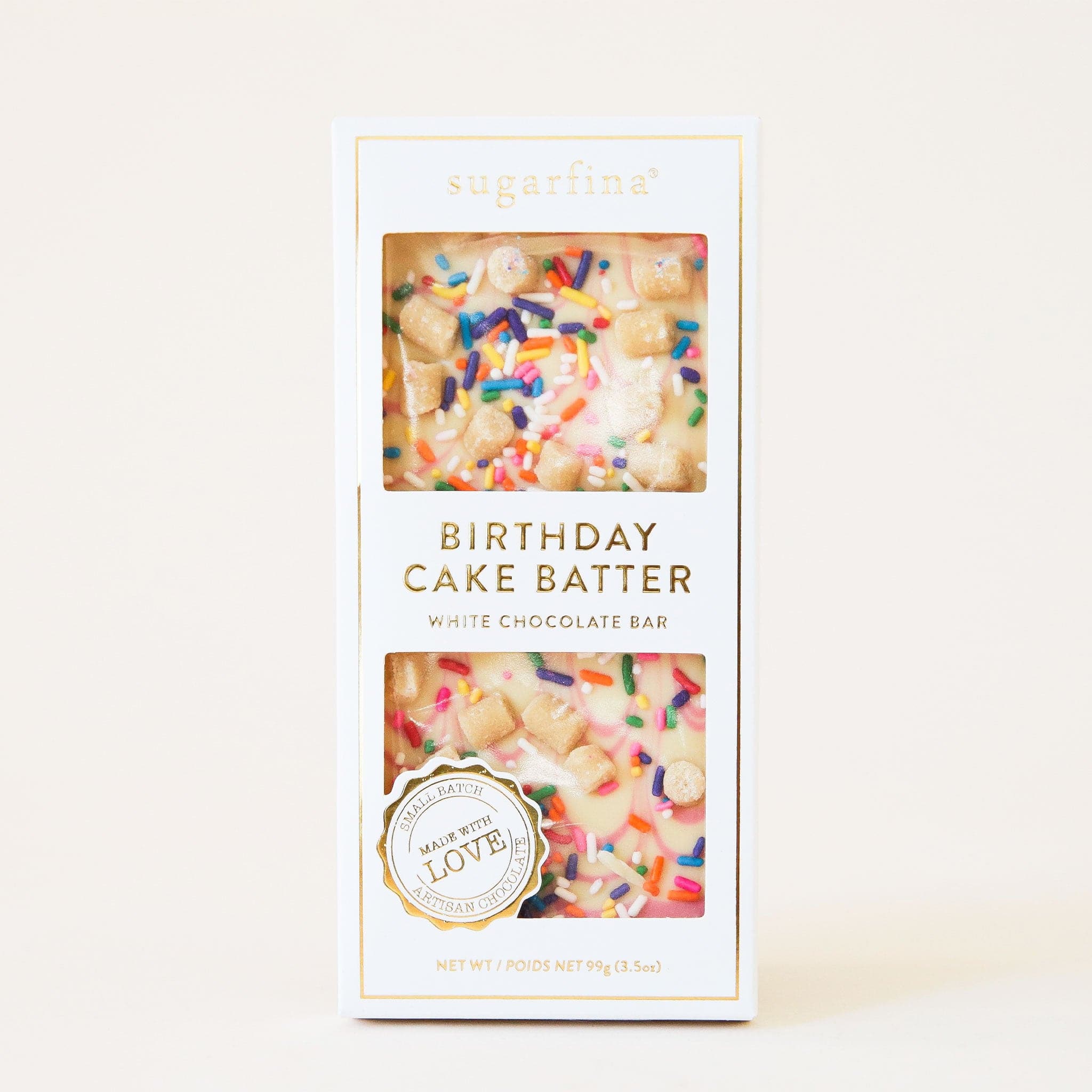 White chocolate bar covered in chunks of cookie dough and rainbow sprinkles. The bar  has white packaging accented with gold foil detailing that reads 'Birthday Cake Batter White Chocolate Bar'.