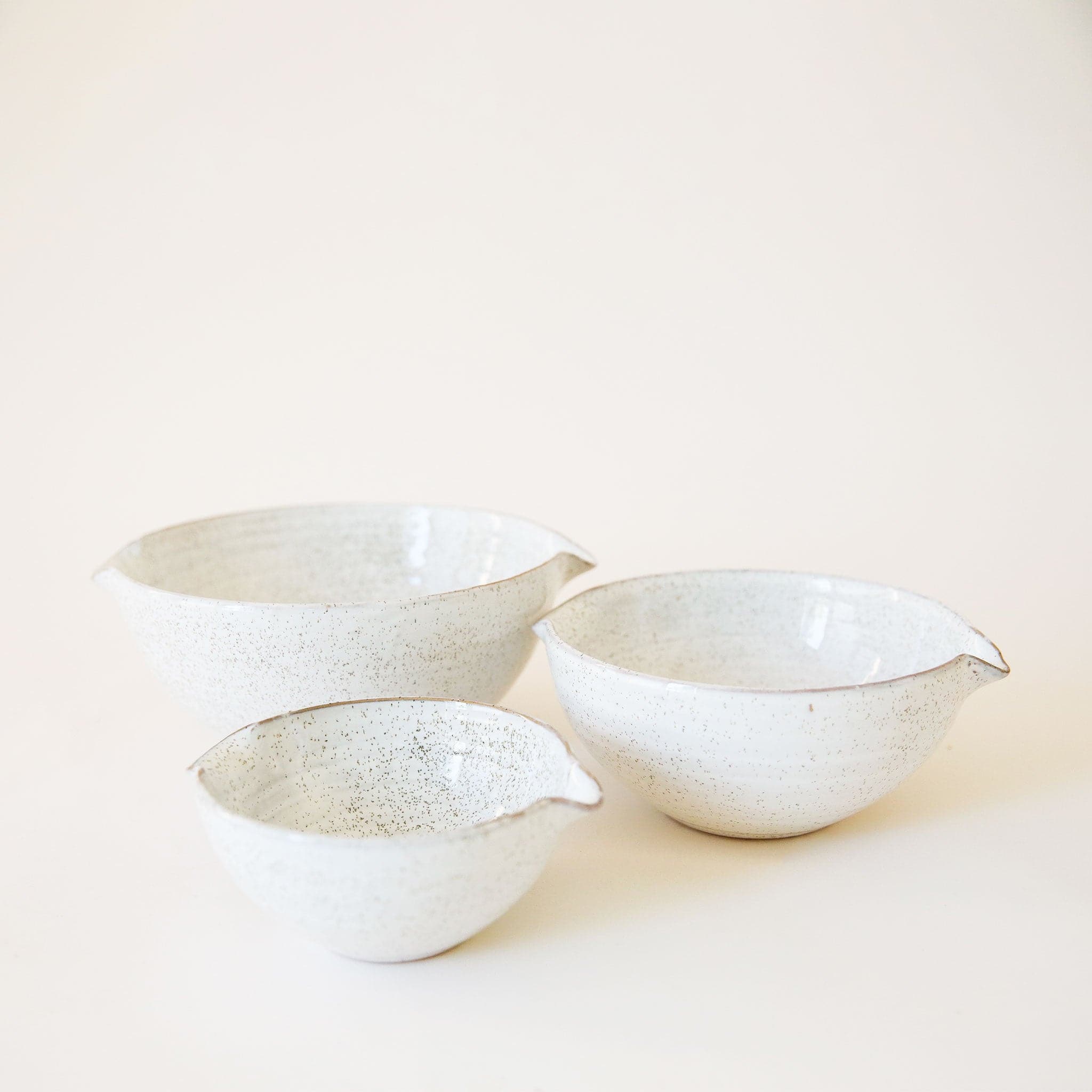 A set of three ceramic bowls nested inside one another. They feature a white base, glossy finish and a tan/brown speckled design. They are rounded bowls with a &#39;v&#39; shaped design on two of the sides making them ideal for pouring if needed.
