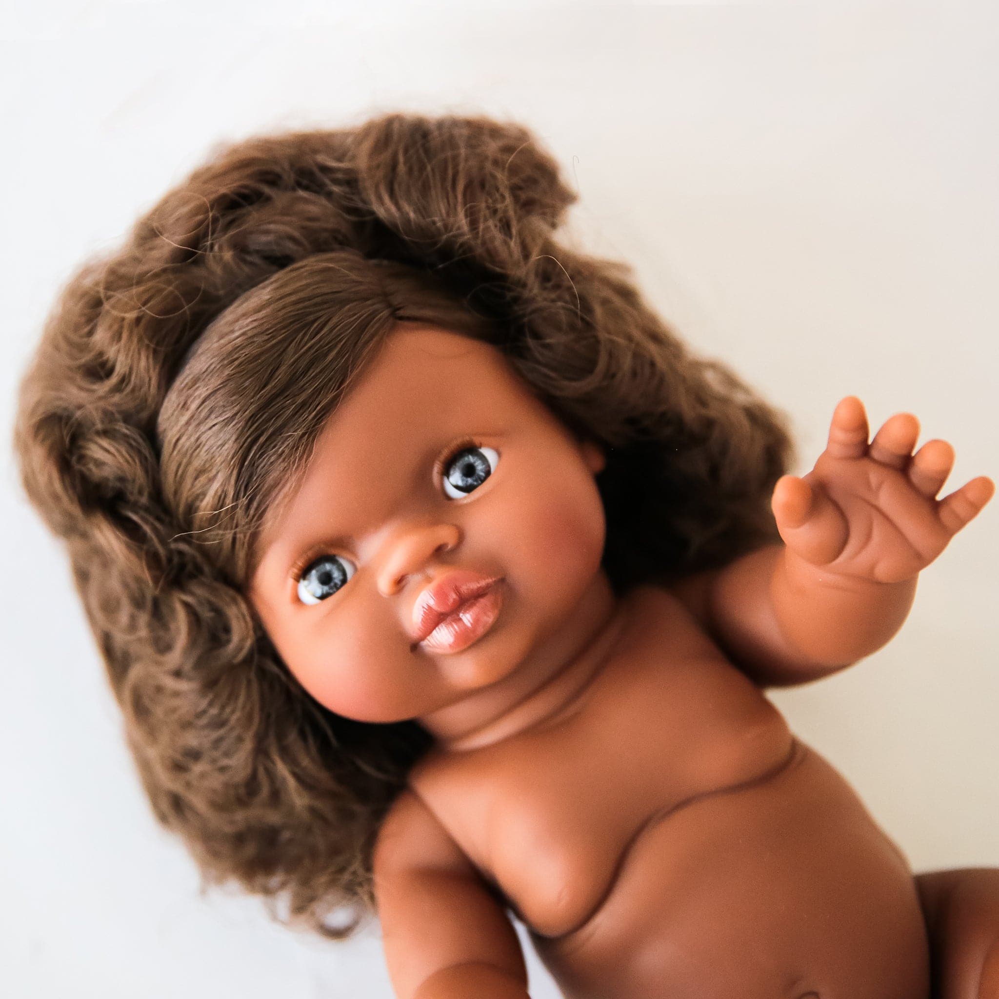 In front of a white background is a baby doll with dark brown curly hair.