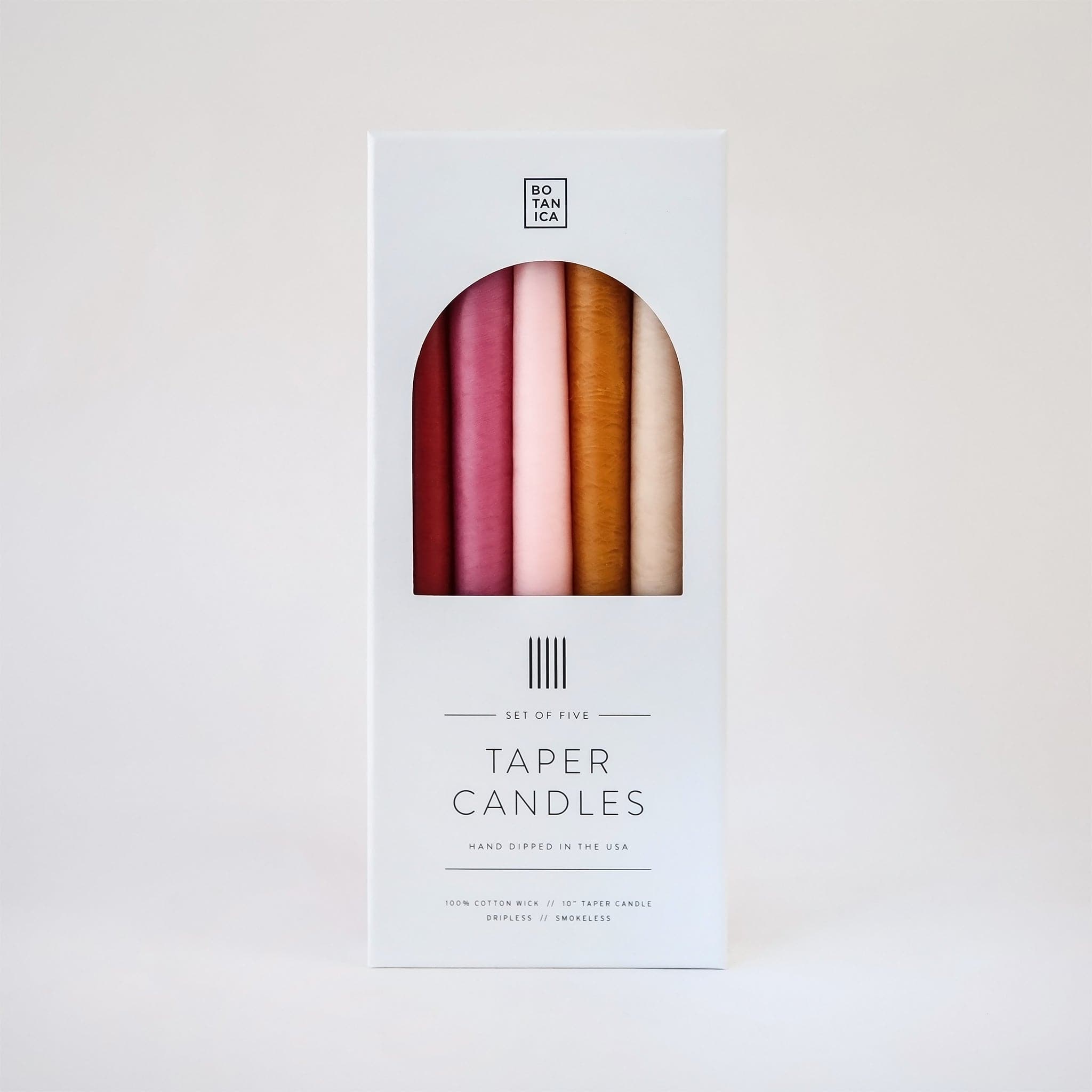 Set of five, 10 inch taper candles that come in warm toned red, pinks and oranges packaged in white Botanica branded box.