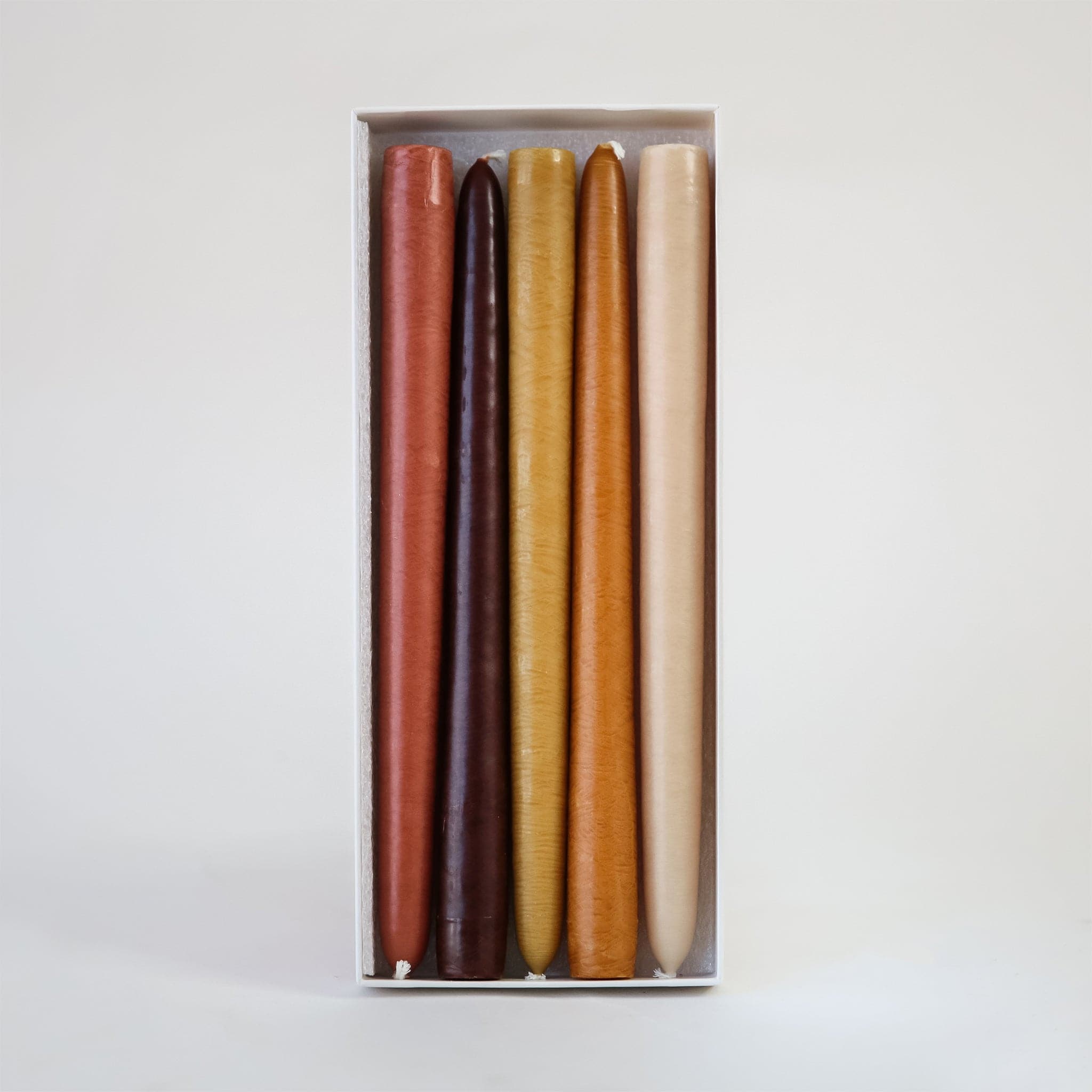 Set of 5 deep warm natural colored 10 inch candles positioned in open white box against white background. 