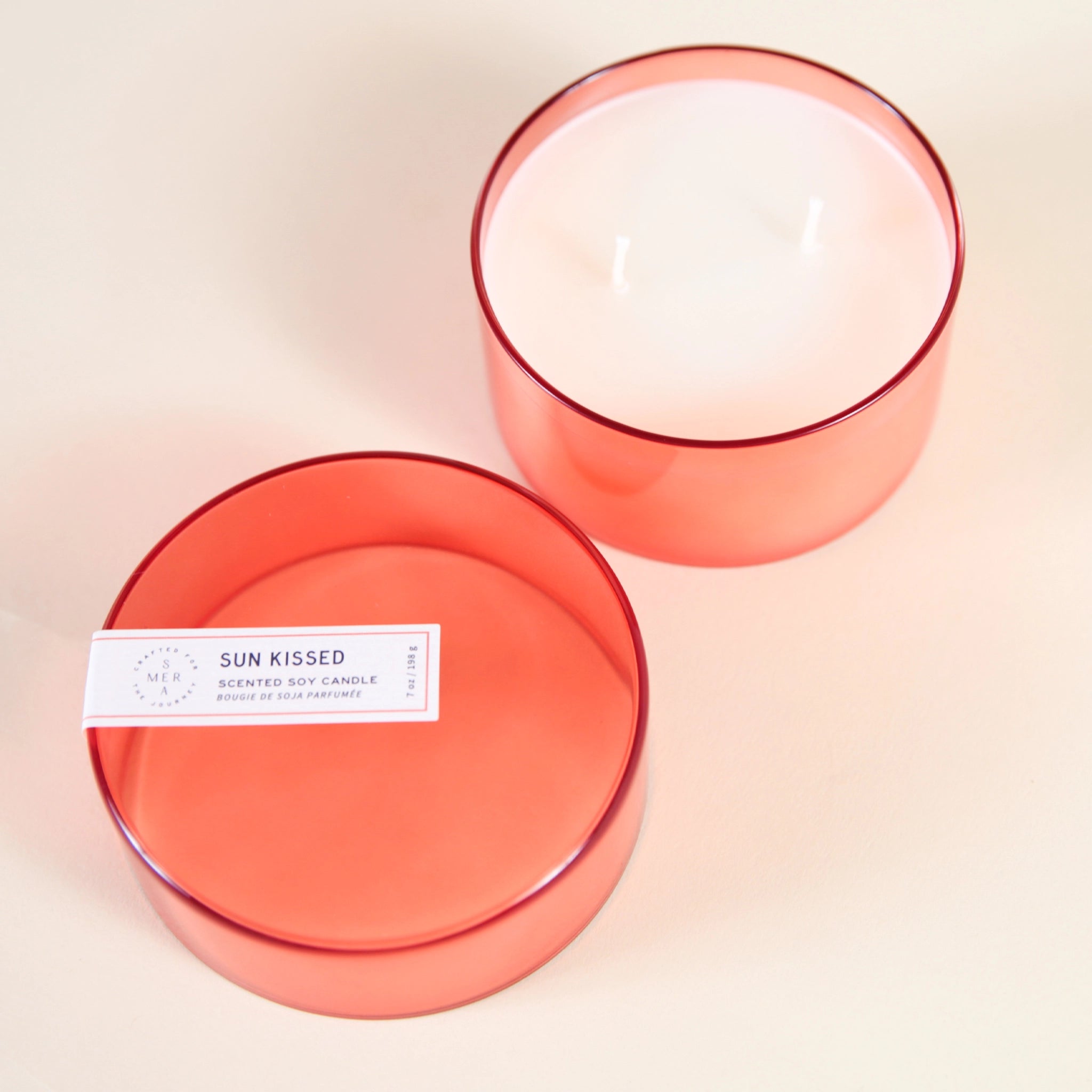 A clear orange/red glass jar candle with white wax and a double wick along with a coordinating glass lid.