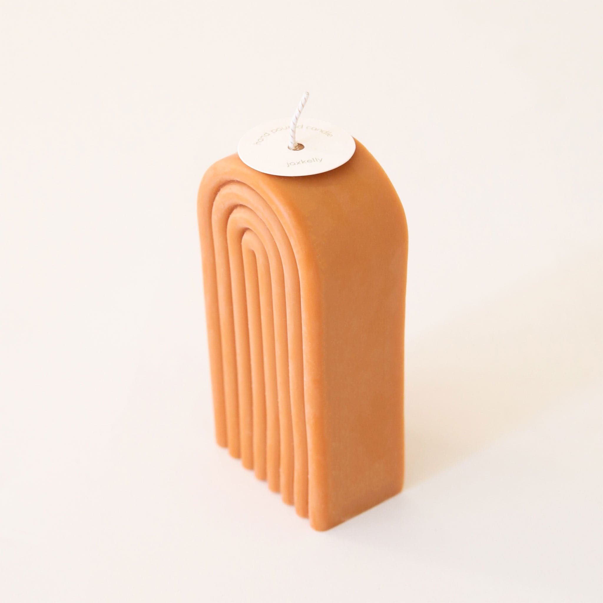 Side angle of single tall, arch shaped candle. The side of the candle is smooth and curved.