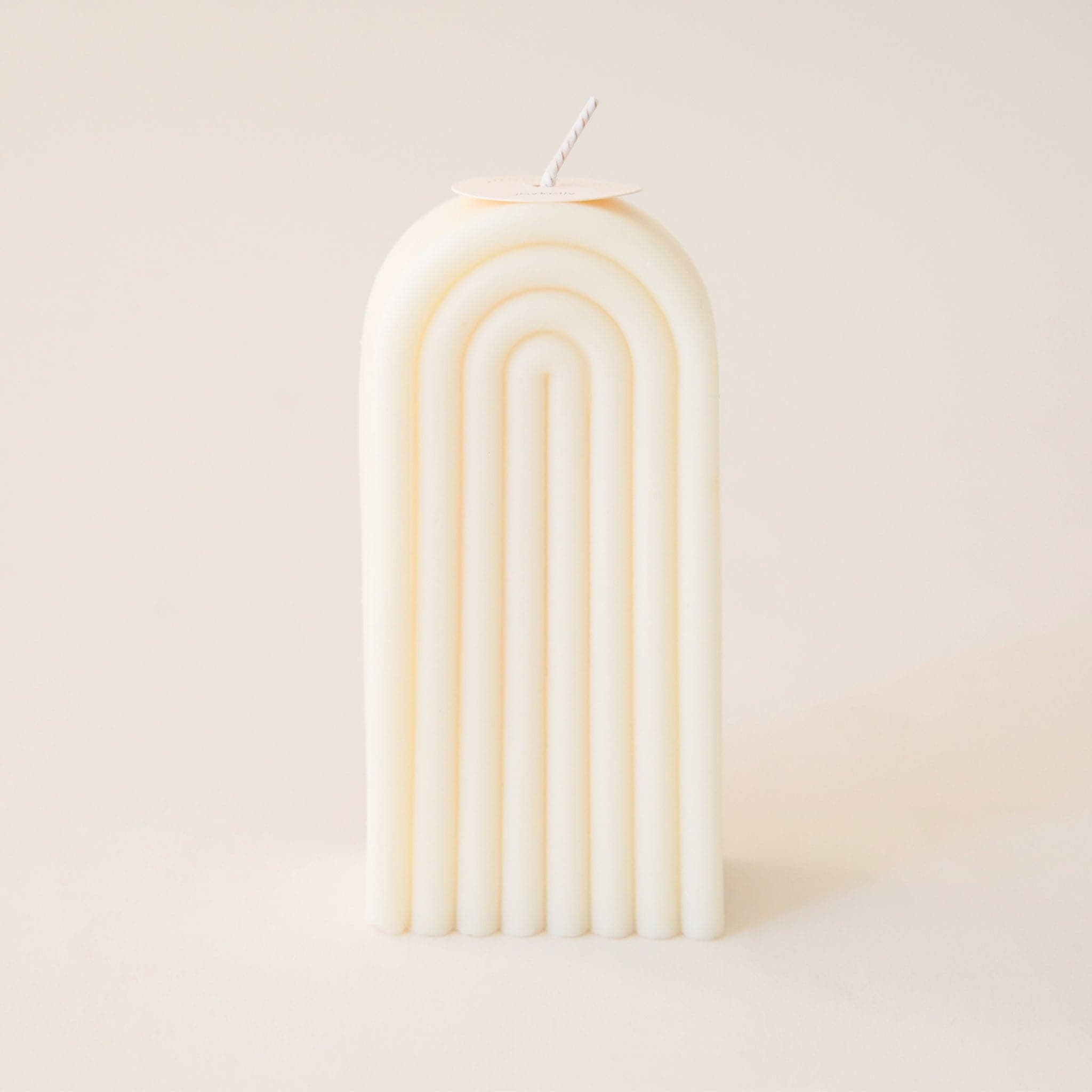 Single tall, arch shaped candle. The candle is carved with rainbow-shaped curves and has a white wick sprouting from the top.